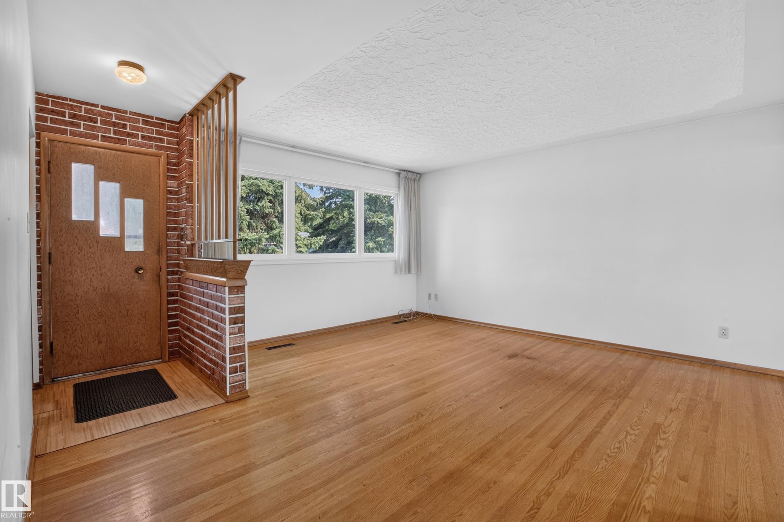 Wood-finish flooring, brick accent wall, wood door with decorative glass inserts, and a three-lite window. - 16009 93A Avenue Nw, Edmonton, AB - Indoor Photo Showing Other Room