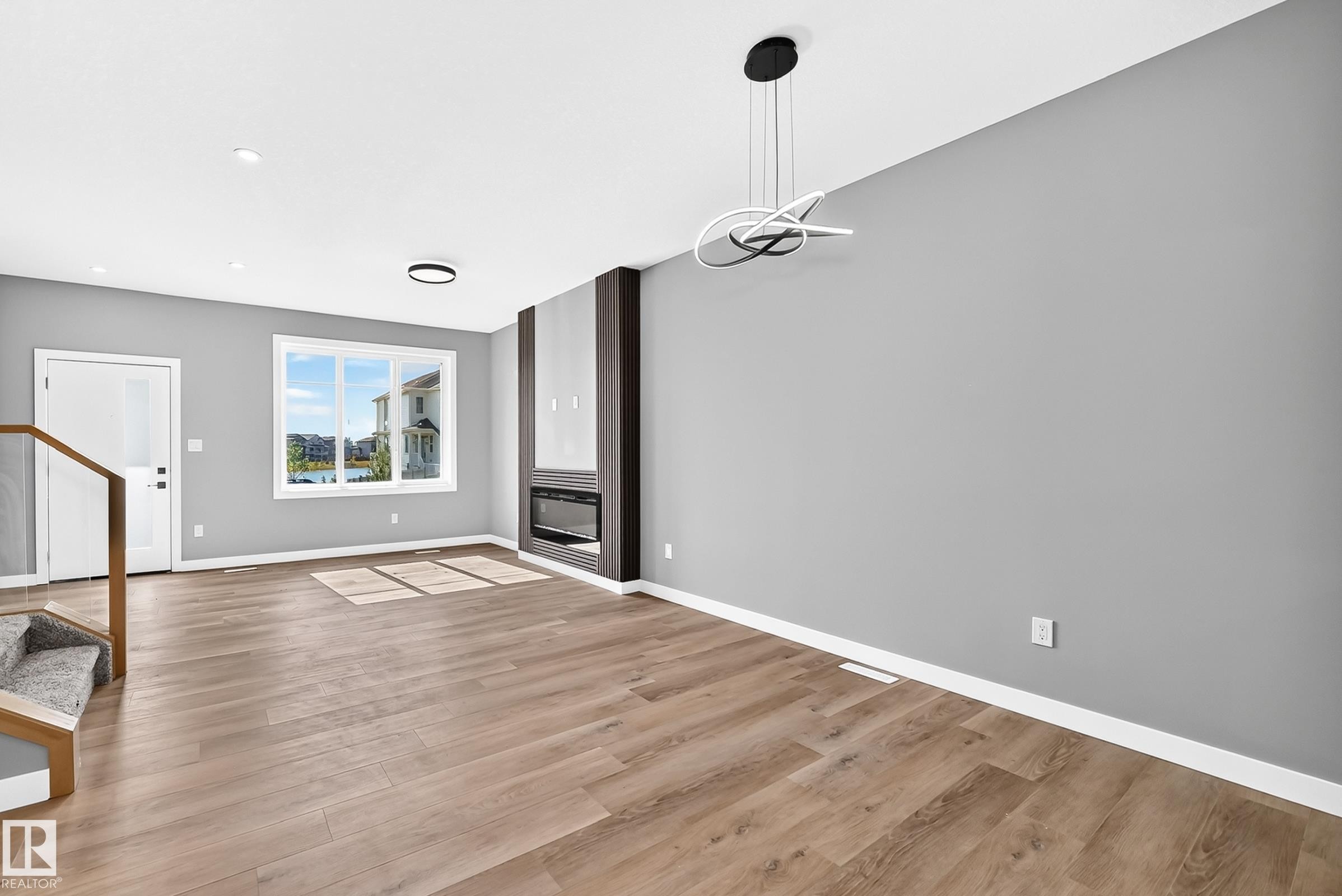 Wood-finish flooring, recessed lighting, modern fireplace with dark wood surround, contemporary pendant light fixture, and a large window - 426 Crystal Creek Link, Leduc, AB - Indoor Photo Showing Other Room