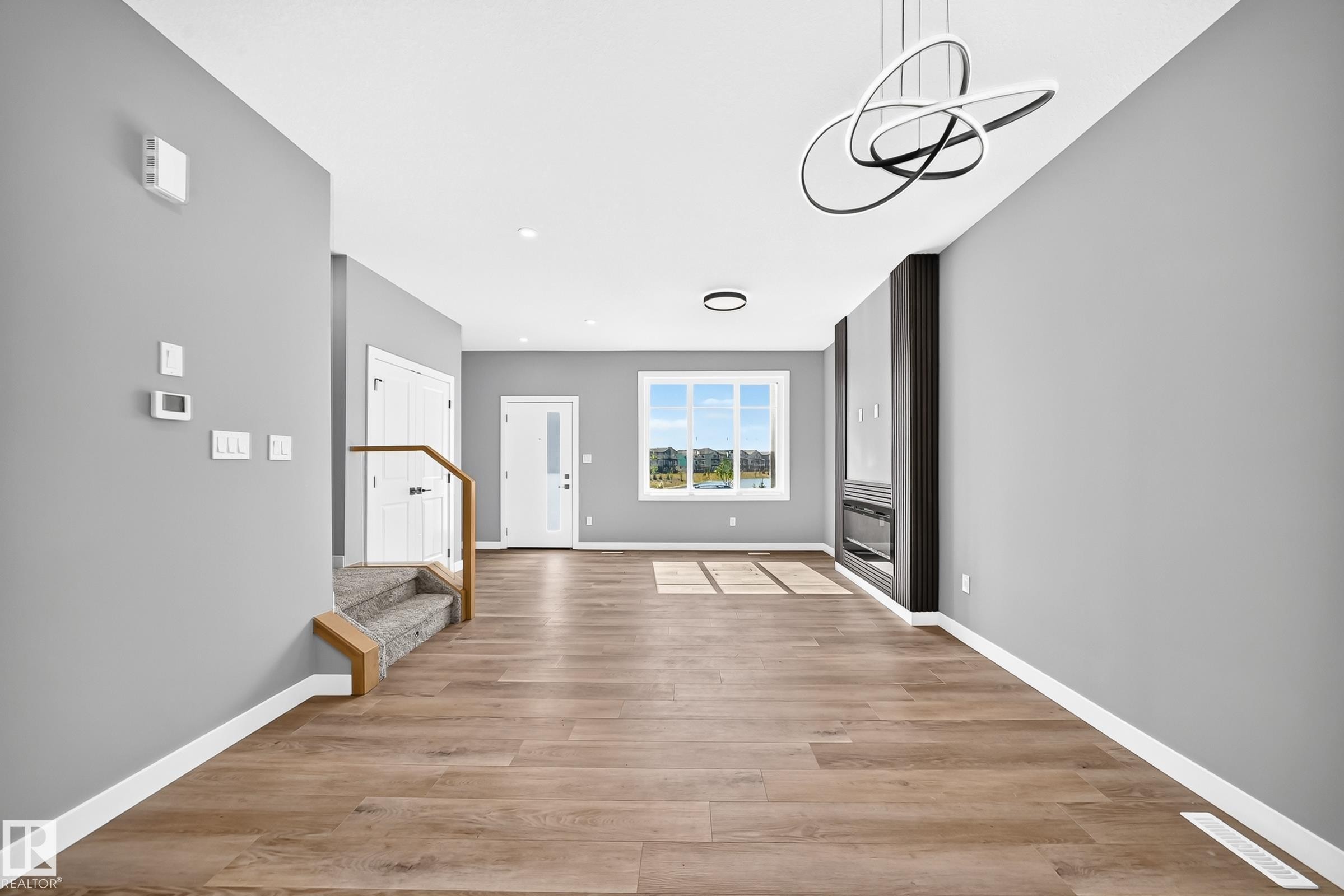 Wood-finish flooring throughout, bright walls, large window, contemporary lighting, and a built-in fireplace feature - 426 Crystal Creek Link, Leduc, AB - Indoor Photo Showing Other Room