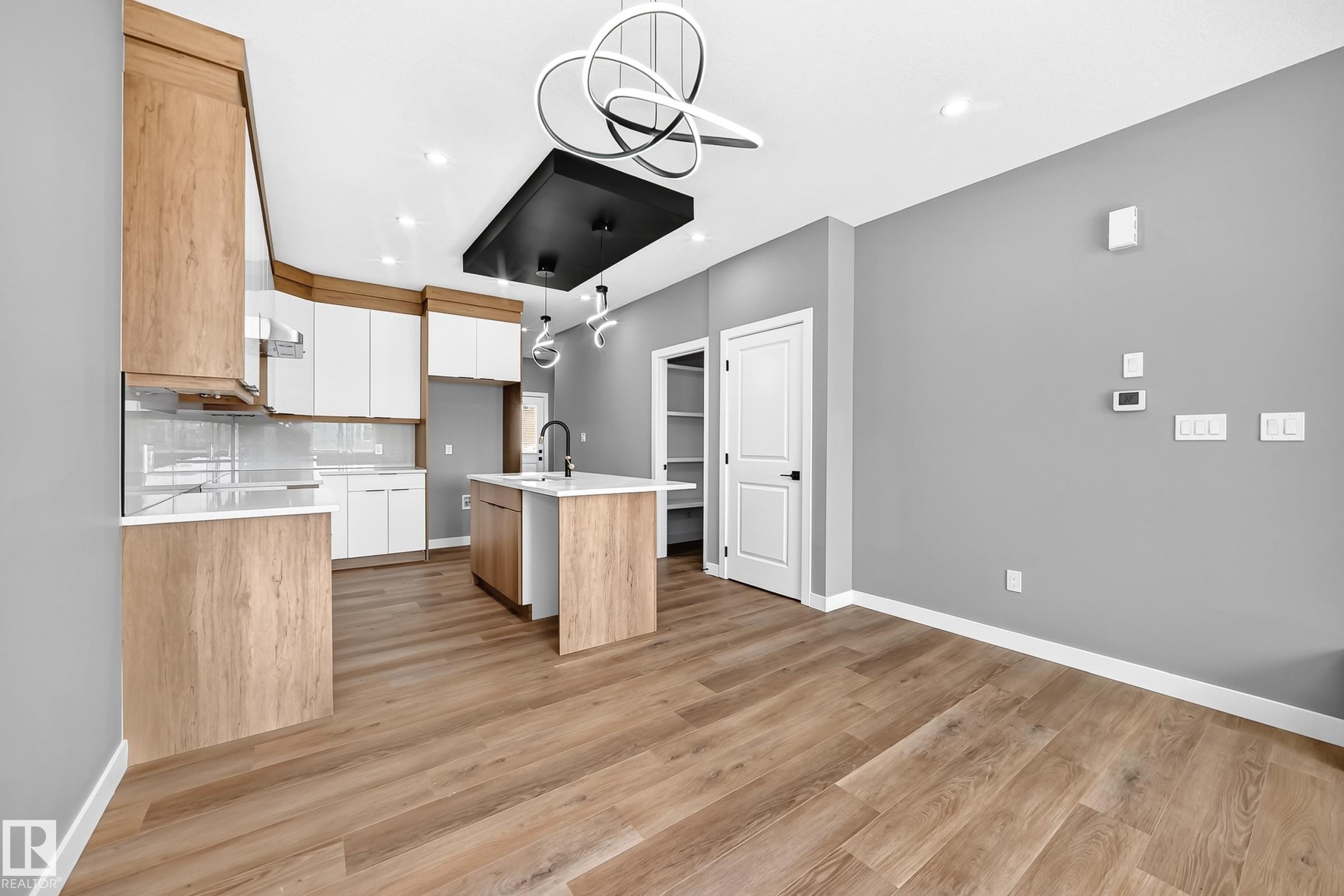 Kitchen featuring wood-finish cabinetry, a central island with a sink, pendant lighting, and wood-finish flooring - 426 Crystal Creek Link, Leduc, AB - Indoor Photo Showing Kitchen