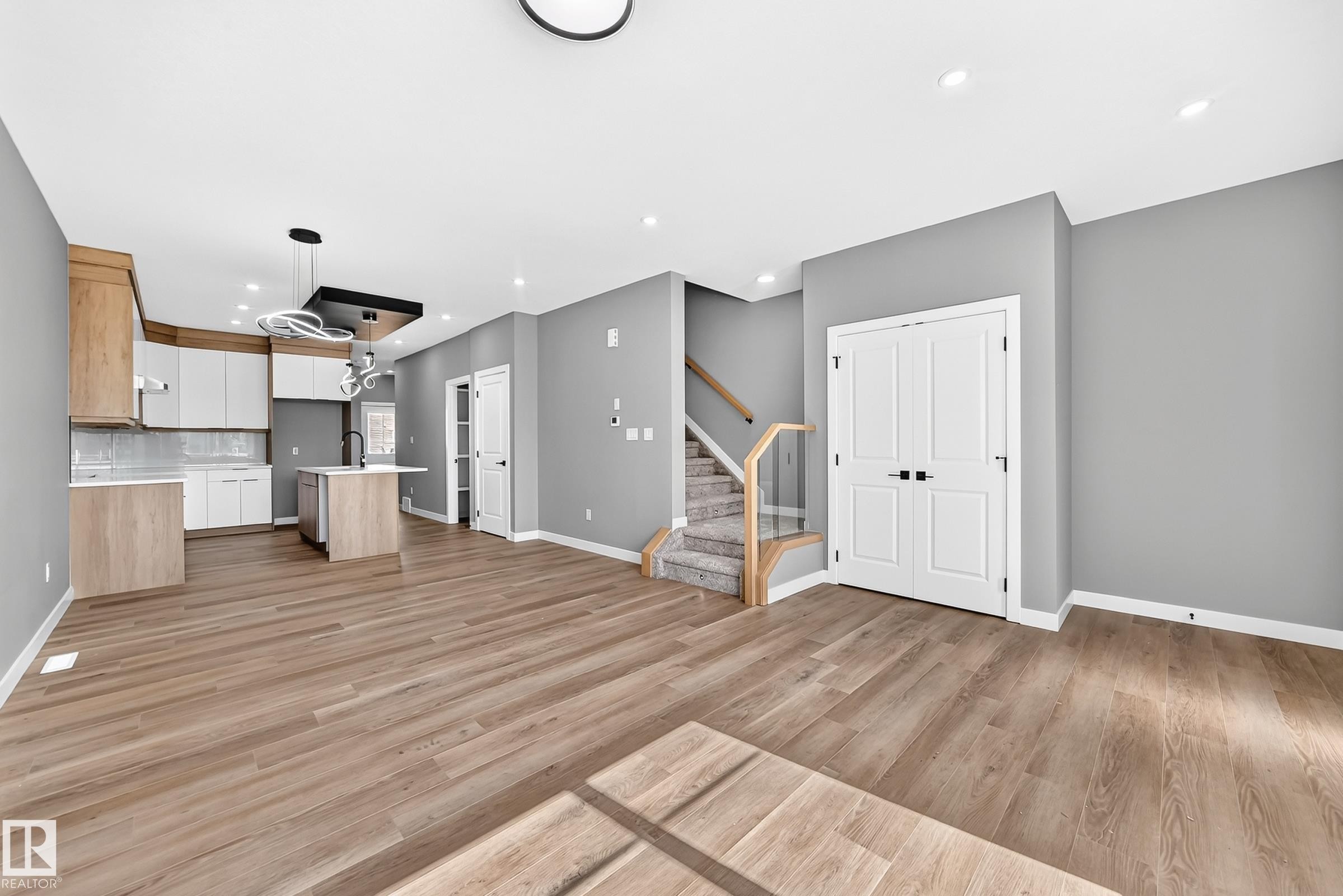 Open-concept living area featuring warm wood-finish flooring, recessed ceiling lighting, and a modern kitchen with light cabinetry and island - 426 Crystal Creek Link, Leduc, AB - Indoor Photo Showing Other Room