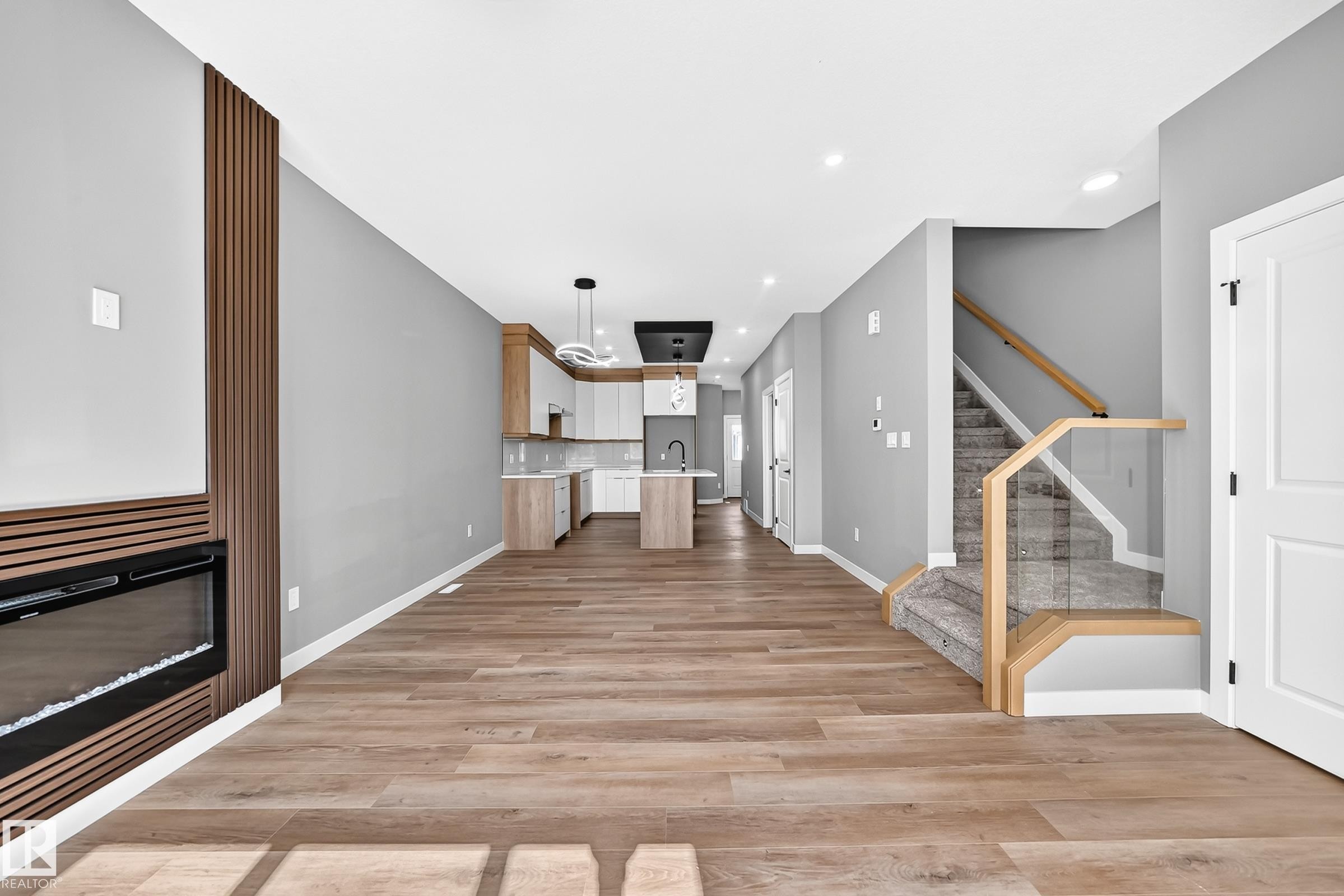 Open-concept living area with wood-finish flooring, a built-in fireplace featuring a slat accent wall, and a modern kitchen with an island - 426 Crystal Creek Link, Leduc, AB - Indoor Photo Showing Other Room