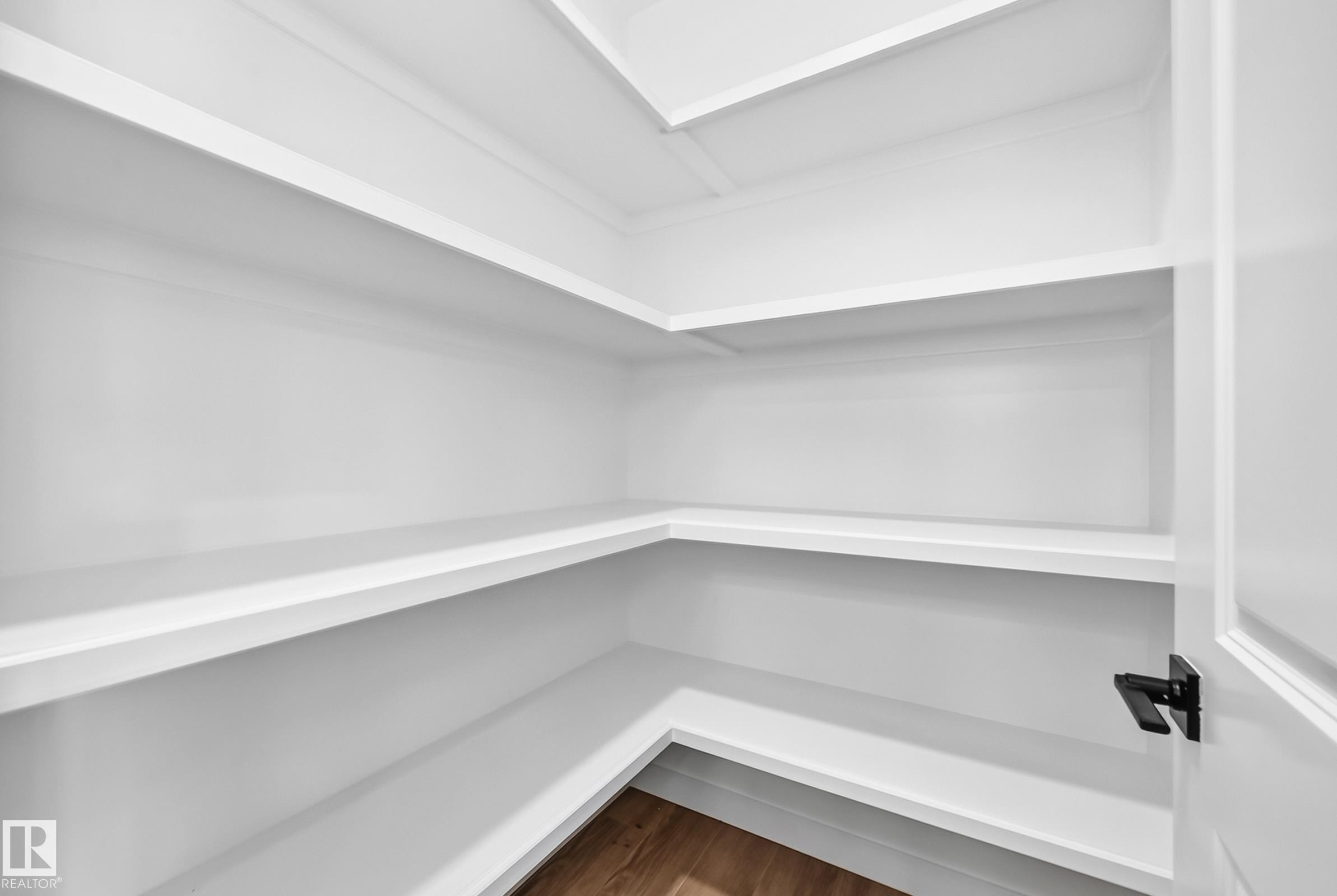 Spacious pantry featuring multiple white shelves, a wood-finish floor, and a white door with a matte black handle - 426 Crystal Creek Link, Leduc, AB - Indoor