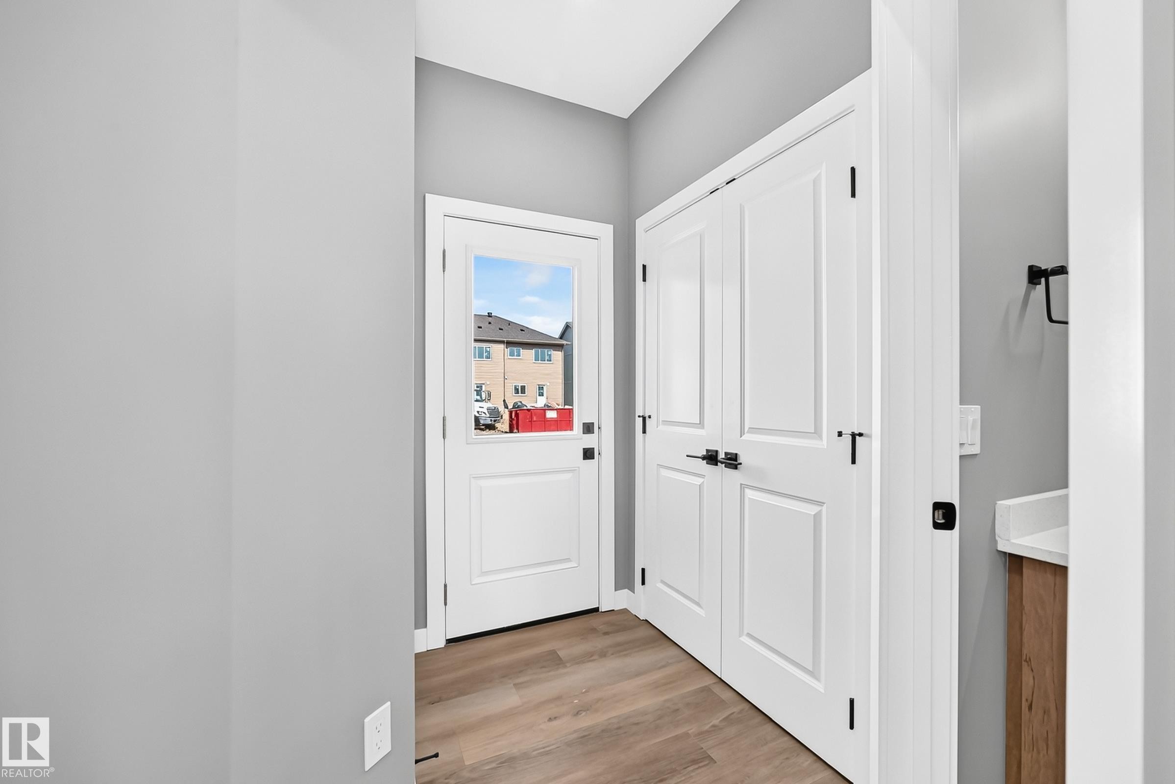Wood-finish flooring, white panel doors with matte black hardware, and a single-pane exterior door - 426 Crystal Creek Link, Leduc, AB - Indoor Photo Showing Other Room