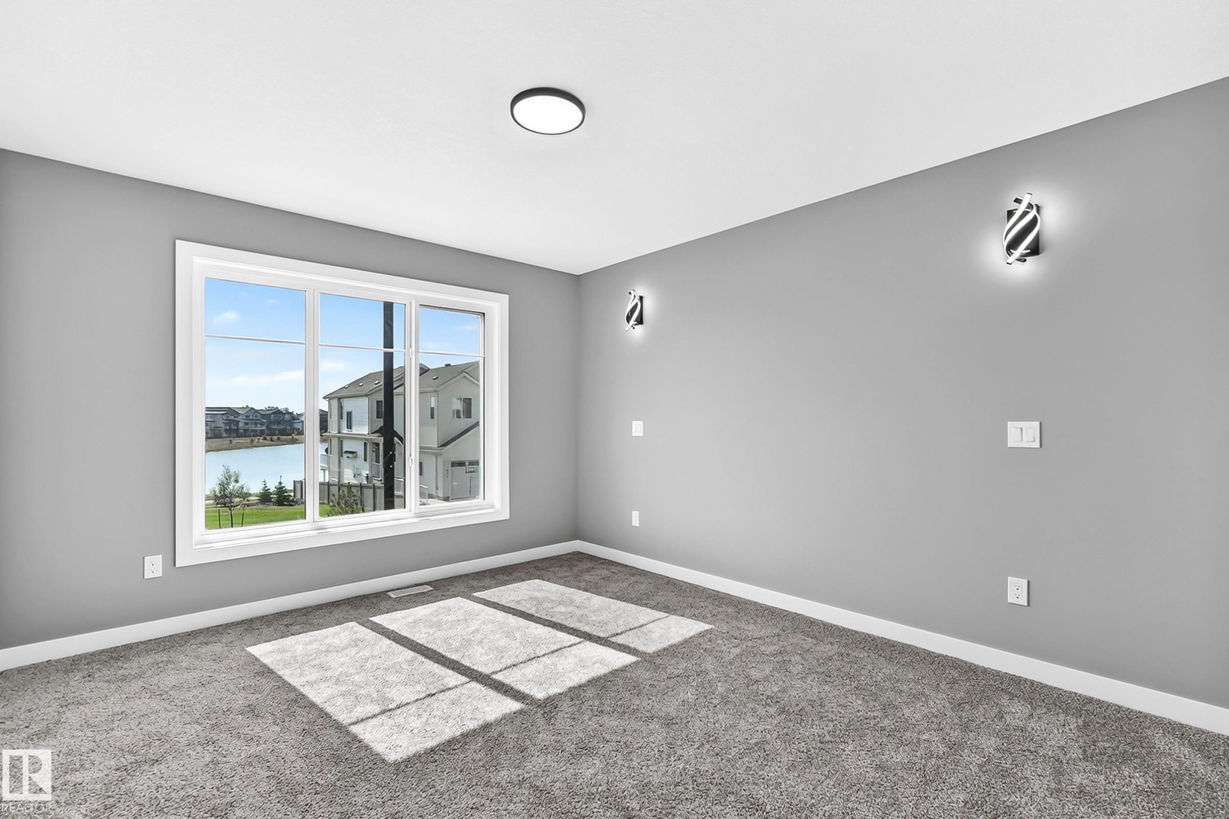 Expansive window with white trim, contemporary wall sconces, ceiling-mounted light fixture, and textured carpeting - 426 Crystal Creek Link, Leduc, AB - Indoor Photo Showing Other Room