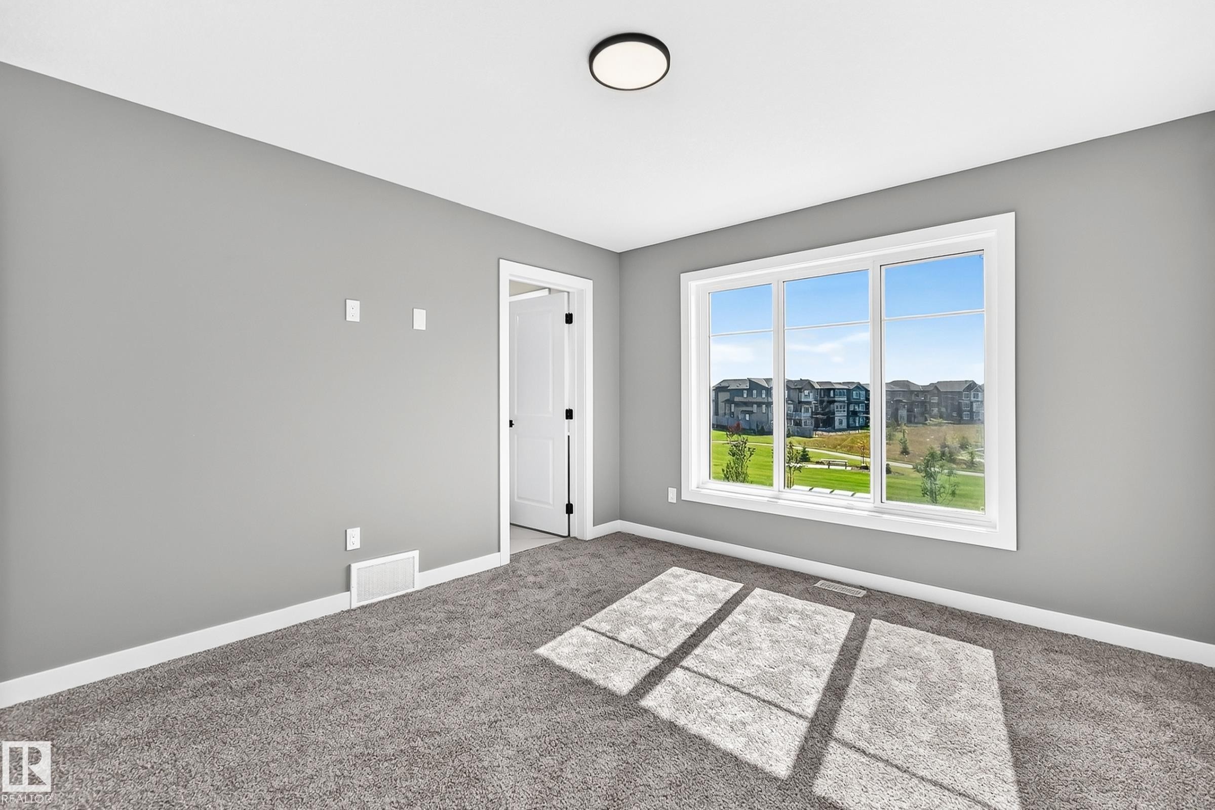 Gray wall finish, white trim, gray carpeting, flush-mount ceiling light, and a large multi-pane window - 426 Crystal Creek Link, Leduc, AB - Indoor Photo Showing Other Room