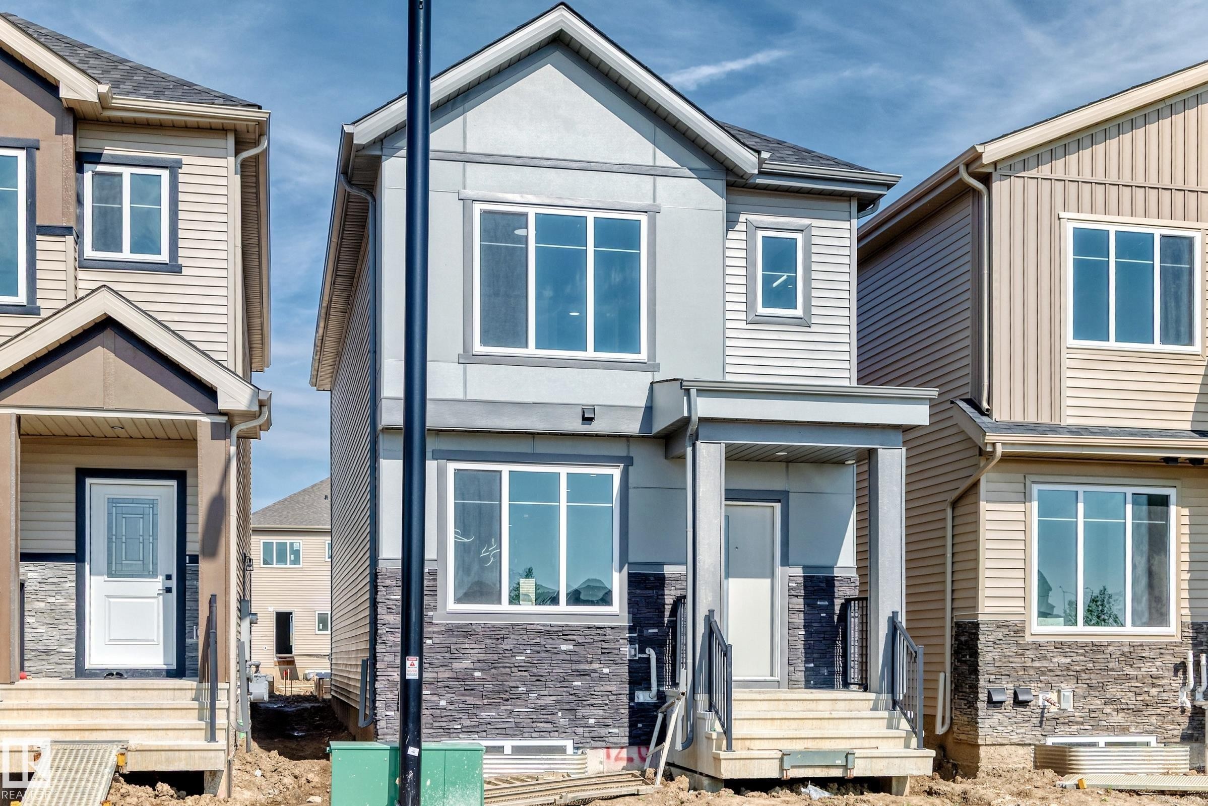 Two-story exterior with a covered entry, stone veneer accent, light gray siding, and multiple windows - 426 Crystal Creek Link, Leduc, AB - Outdoor With Facade