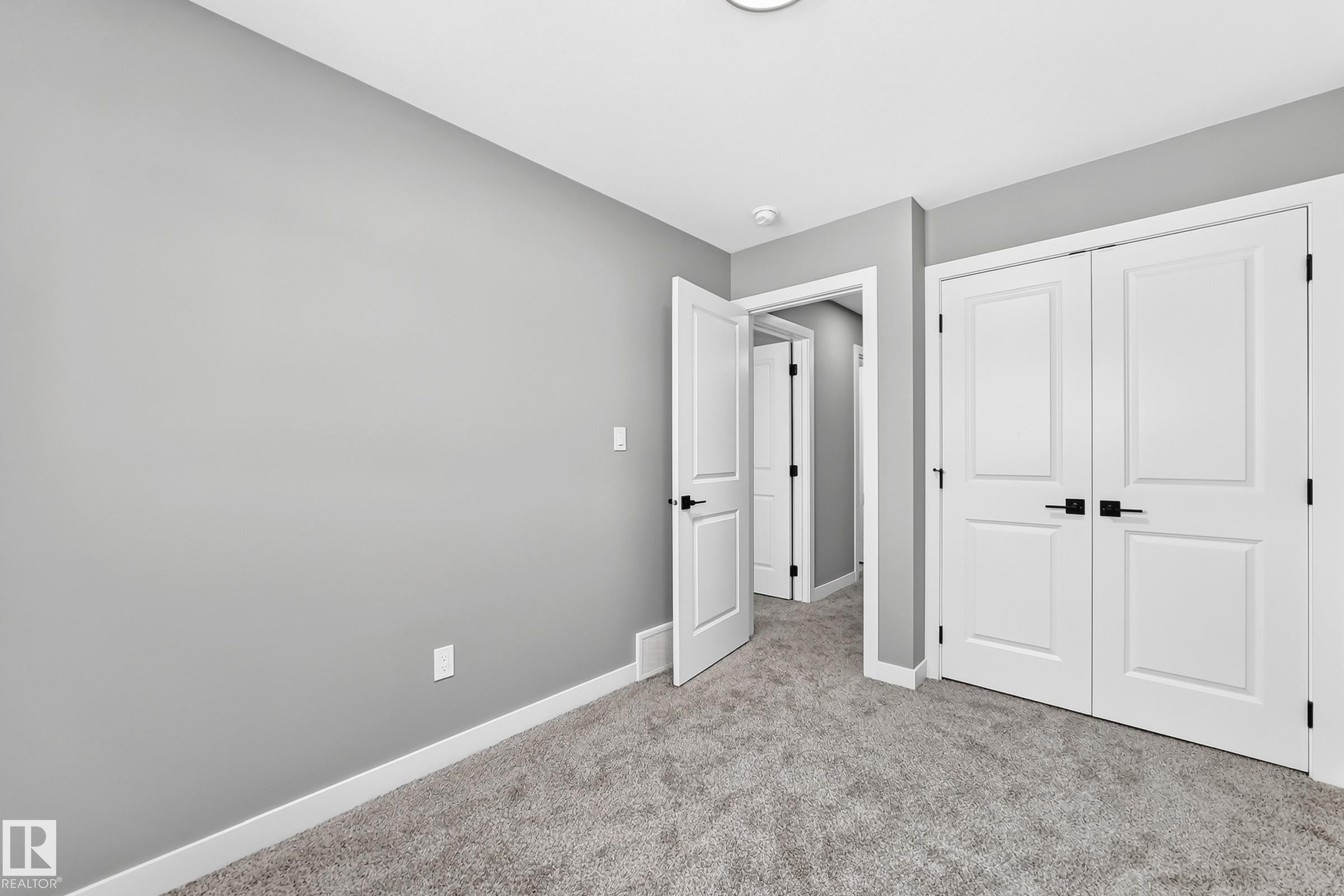 Plush carpeting, light grey wall paint, crisp white trim, and white paneled doors with black hardware - 426 Crystal Creek Link, Leduc, AB - Indoor Photo Showing Other Room