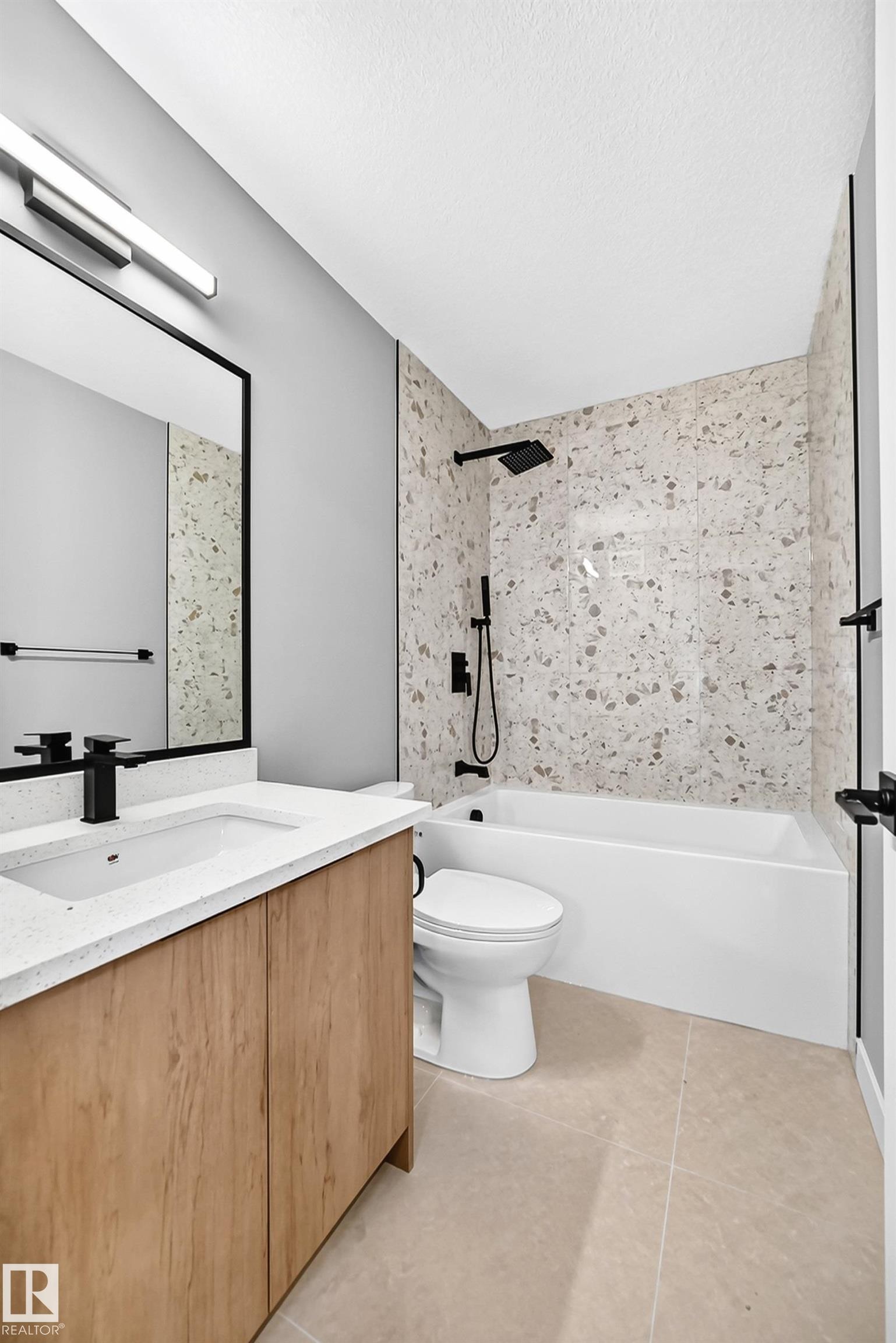 Wood-finish vanity with a white countertop and integrated sink, matte black faucet, full-width mirror, light-toned floor tile, and a tiled shower surround with a matte black shower head and controls - 426 Crystal Creek Link, Leduc, AB - Indoor Photo Showing Bathroom