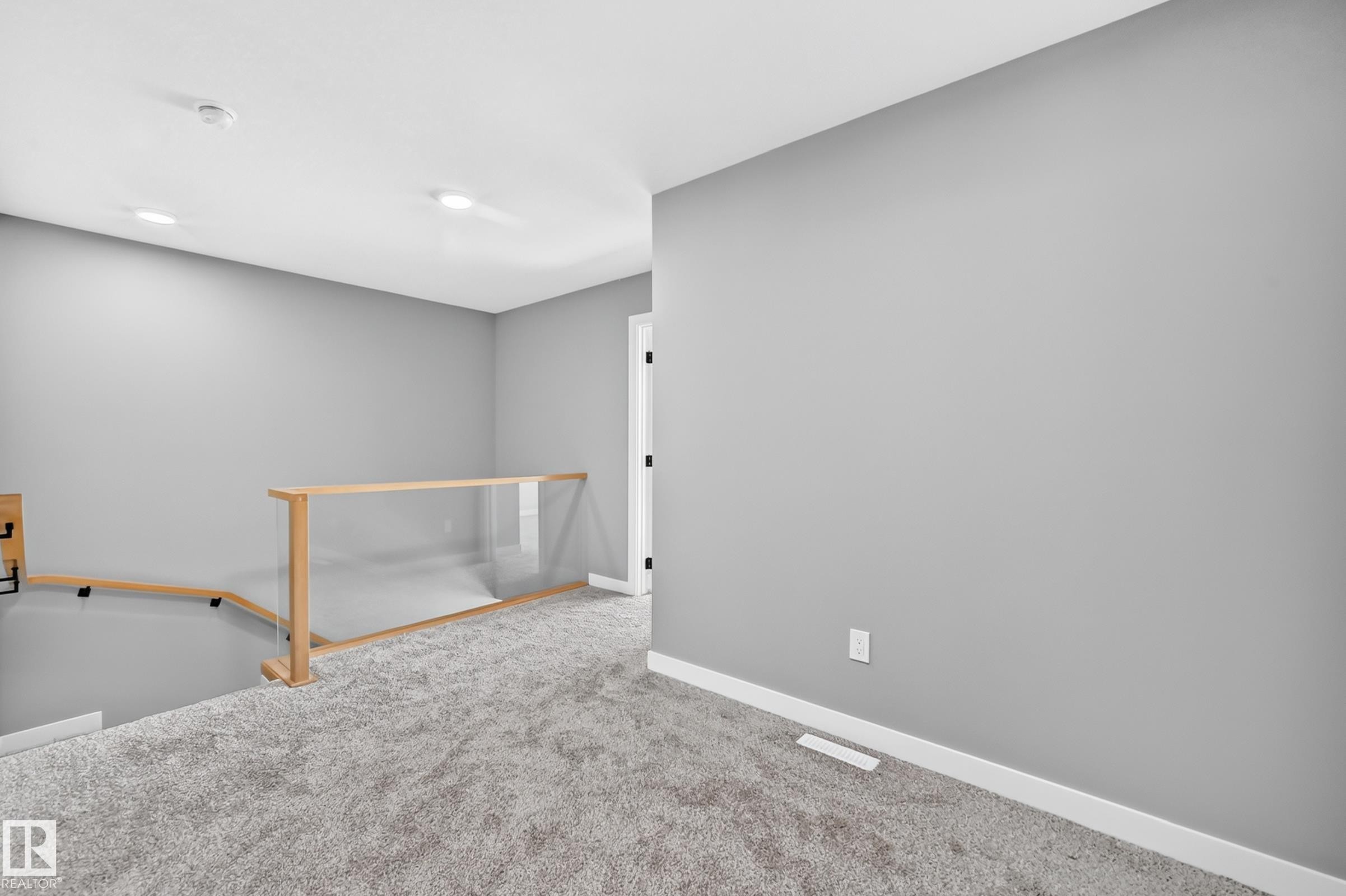 Gray carpeted landing featuring a wood and glass railing system, recessed lighting, and a white interior door with black hardware - 426 Crystal Creek Link, Leduc, AB - Indoor Photo Showing Other Room