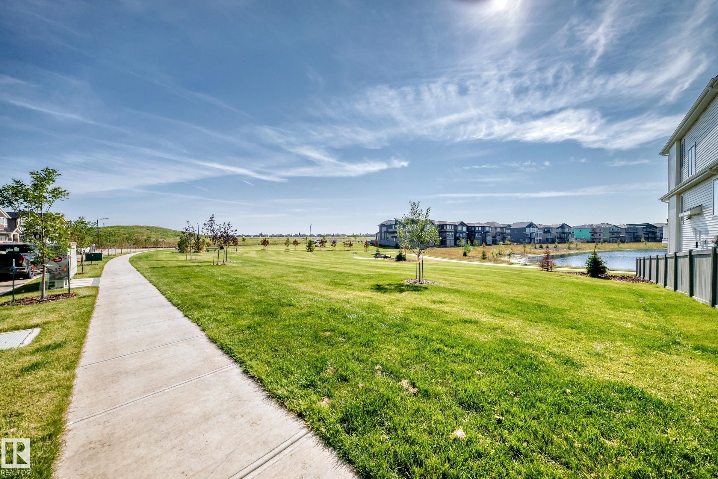 Expansive green space featuring a paved walking path, mature trees, and a tranquil pond - 426 Crystal Creek Link, Leduc, AB - Outdoor With View