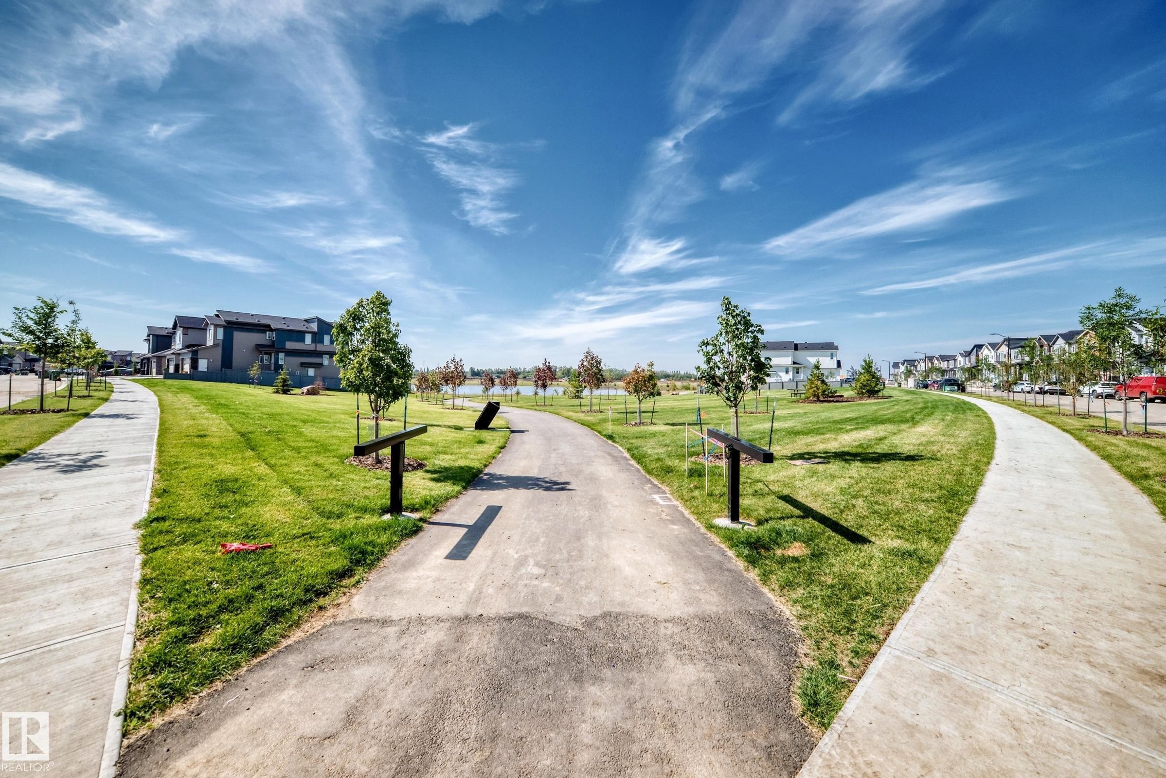 Expansive green space featuring paved pedestrian paths, mature trees, and nearby residential structures - 426 Crystal Creek Link, Leduc, AB - Outdoor With View