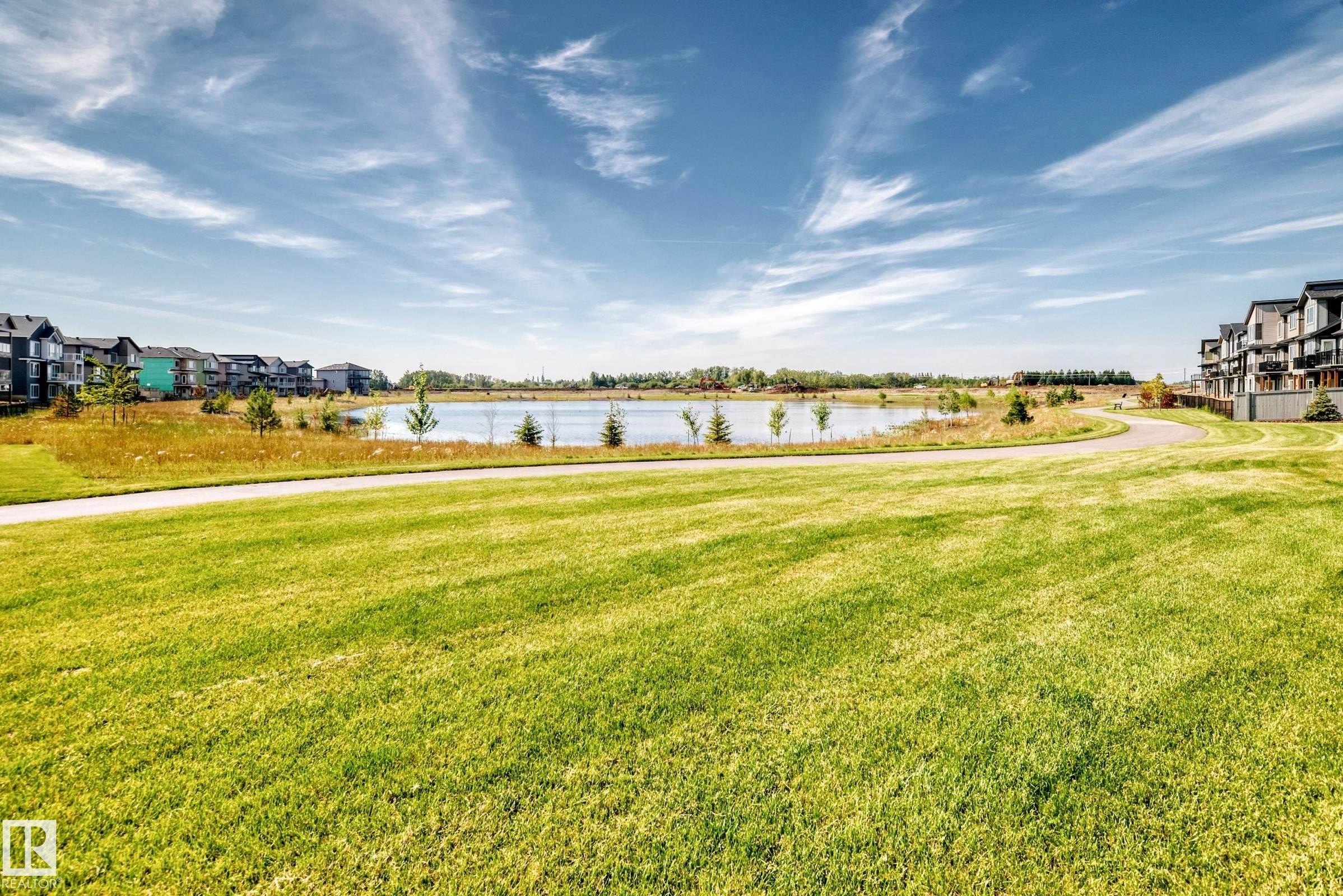 Expansive green space featuring a paved pathway, a tranquil pond, and contemporary multi-story residences - 426 Crystal Creek Link, Leduc, AB - Outdoor With View