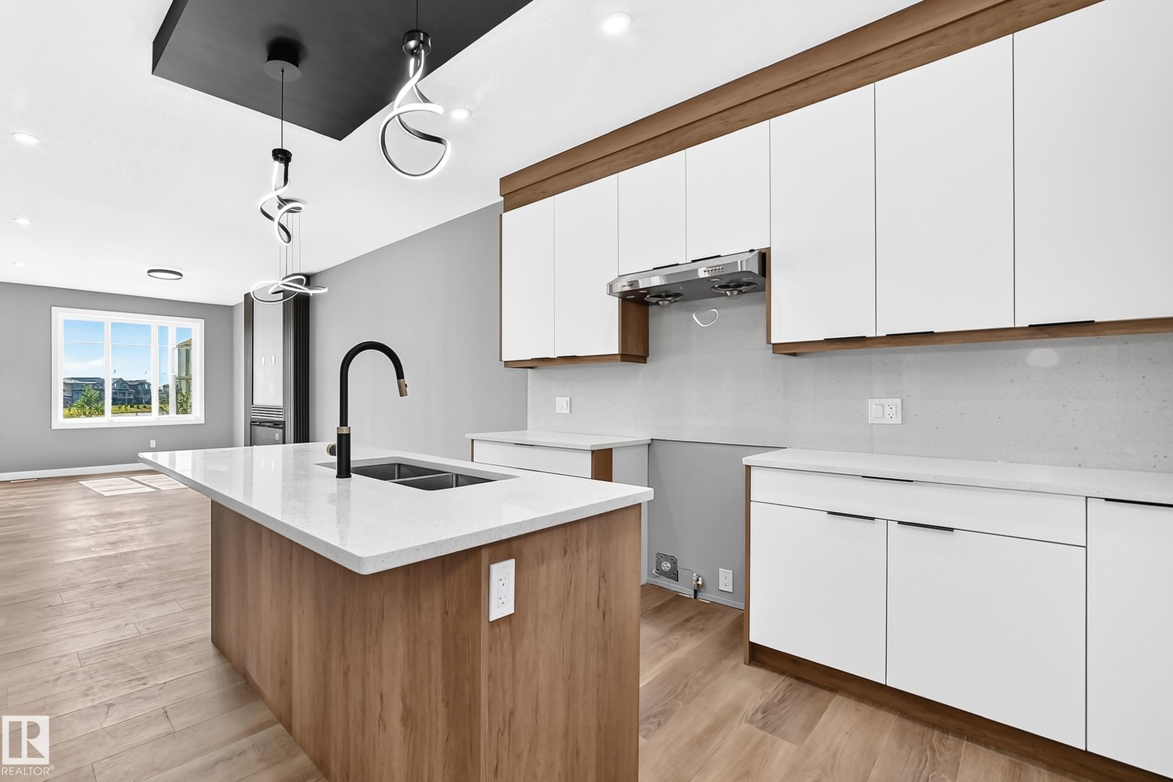 Kitchen island with a built-in sink and matte black faucet, complemented by white countertops and wood-finish cabinetry - 426 Crystal Creek Link, Leduc, AB - Indoor Photo Showing Kitchen With Double Sink