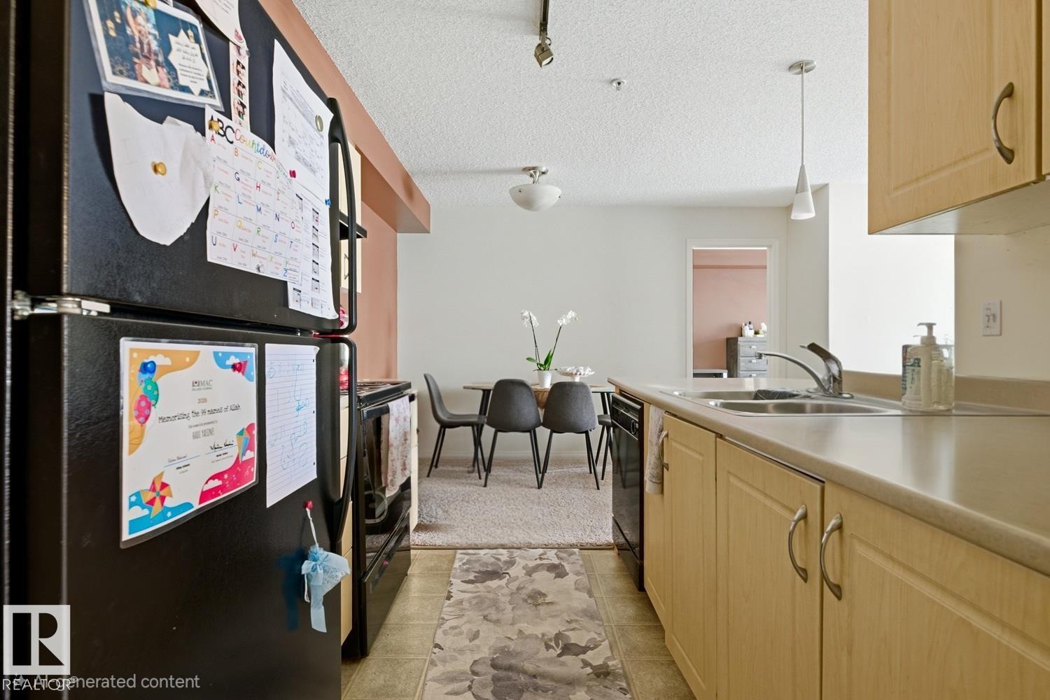 Kitchen featuring wood-finish cabinetry, a double basin stainless steel sink, and light-toned countertops - #106 13907 136 St Nw, Edmonton, AB - Indoor Photo Showing Kitchen With Double Sink