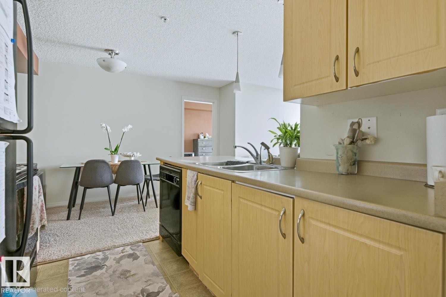 Kitchen featuring wood-finish cabinetry, stainless steel sink, and light-toned countertops - #106 13907 136 St Nw, Edmonton, AB - Indoor Photo Showing Kitchen With Double Sink