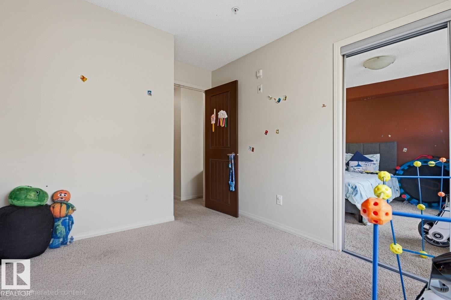 Mirrored closet doors, flush-mount ceiling light, paneled interior door, and neutral-toned carpeting - #106 13907 136 St Nw, Edmonton, AB - Indoor Photo Showing Other Room