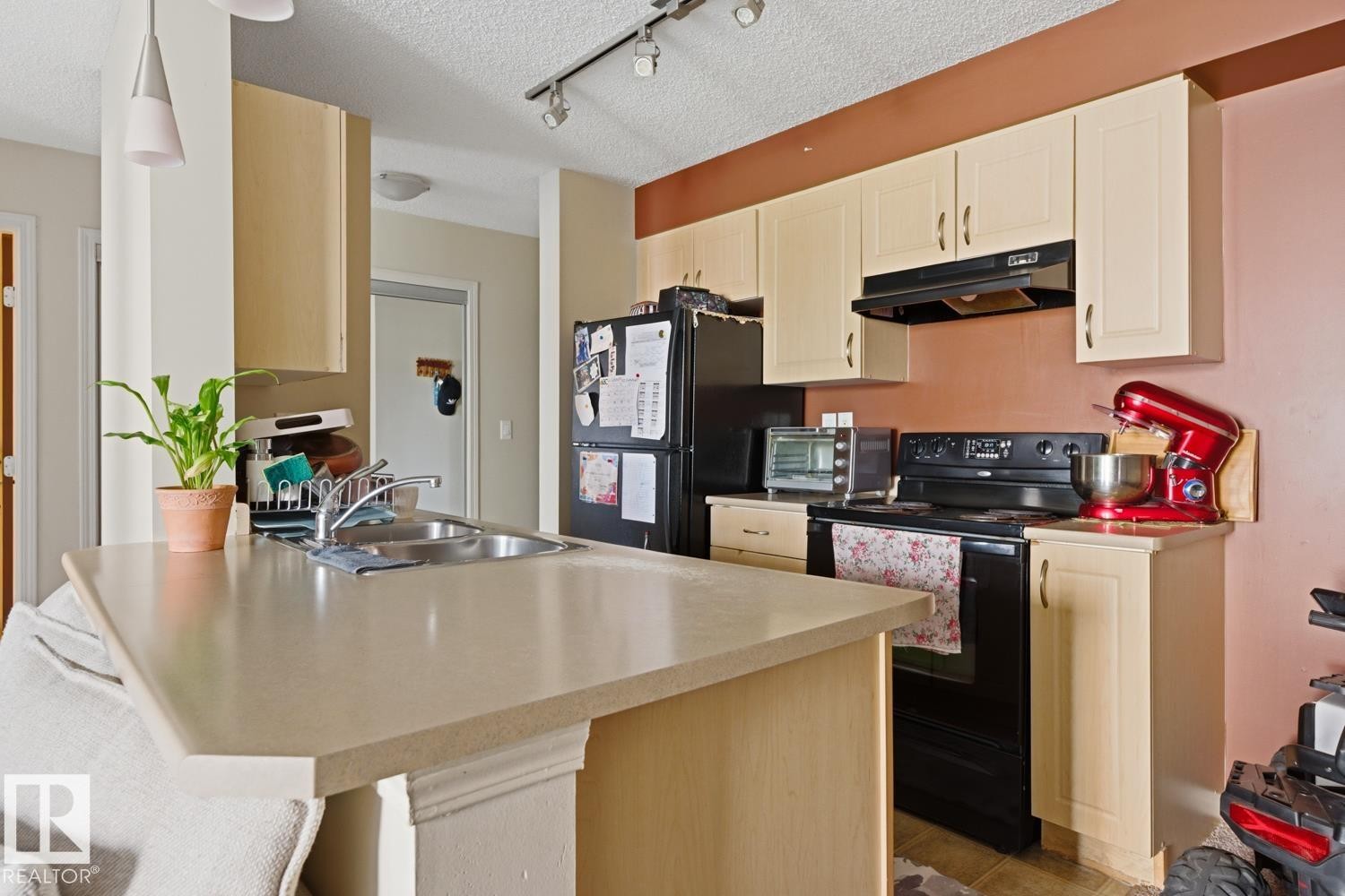 Kitchen featuring light-toned cabinetry, a stainless steel sink, black appliances, and track lighting - #106 13907 136 St Nw, Edmonton, AB - Indoor Photo Showing Kitchen With Double Sink
