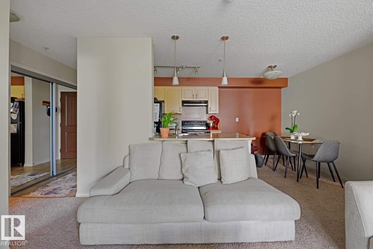 Open-concept living area featuring a kitchen pass-through with pendant lighting, light-toned cabinetry, and dark kitchen appliances - #106 13907 136 St Nw, Edmonton, AB - Indoor
