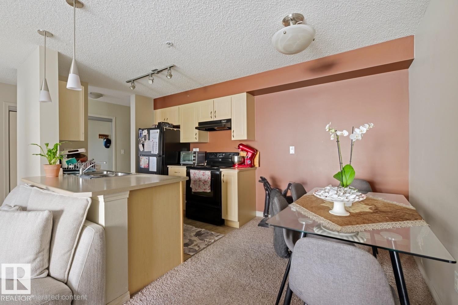 Kitchen featuring light-toned cabinetry, a double basin stainless steel sink, black appliances, and pendant lighting - #106 13907 136 St Nw, Edmonton, AB - Indoor