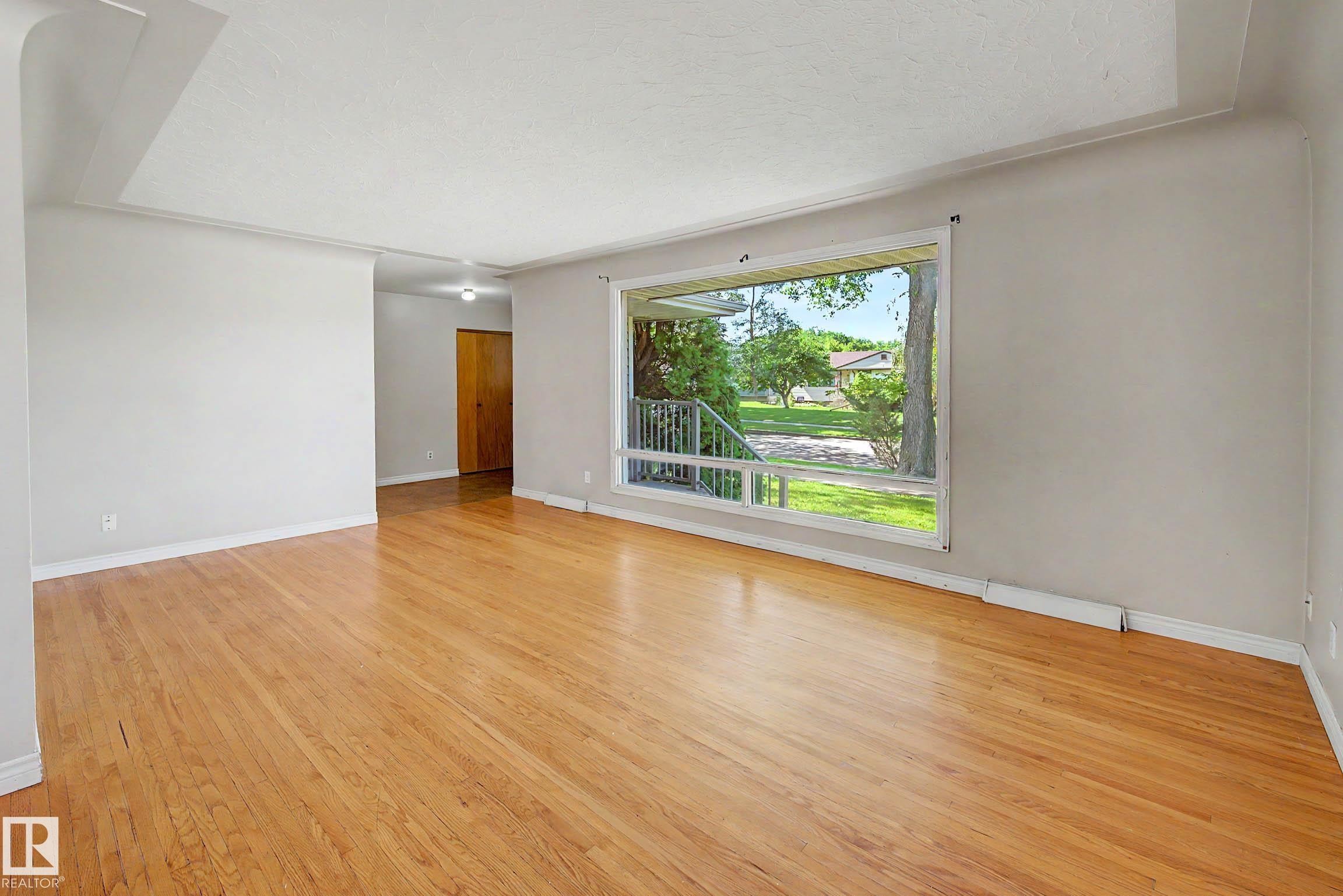Hardwood flooring, light gray wall finishes, a large picture window, and a wood-finish interior door - 9723 76 Street Nw, Edmonton, AB - Indoor