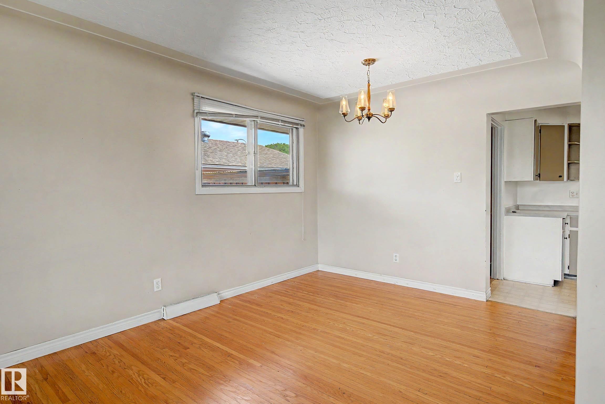 Hardwood flooring, classic chandelier, window with natural light, textured tray ceiling, and crown molding - 9723 76 Street Nw, Edmonton, AB - Indoor Photo Showing Other Room