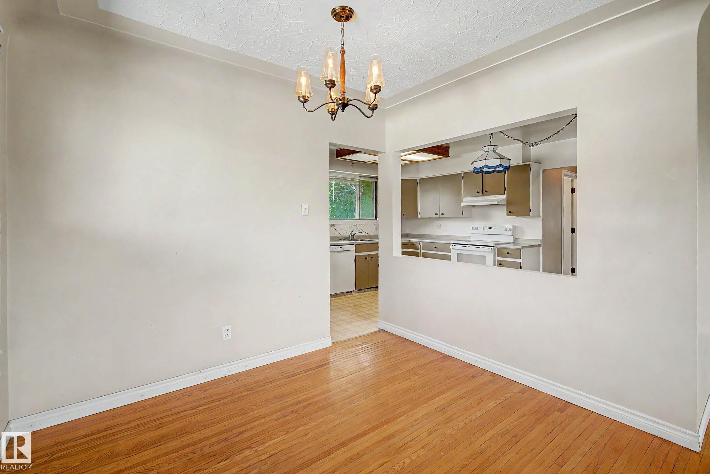 Wood-finish flooring, overhead chandelier, and a kitchen pass-through window with an integrated pendant light - 9723 76 Street Nw, Edmonton, AB - Indoor Photo Showing Kitchen