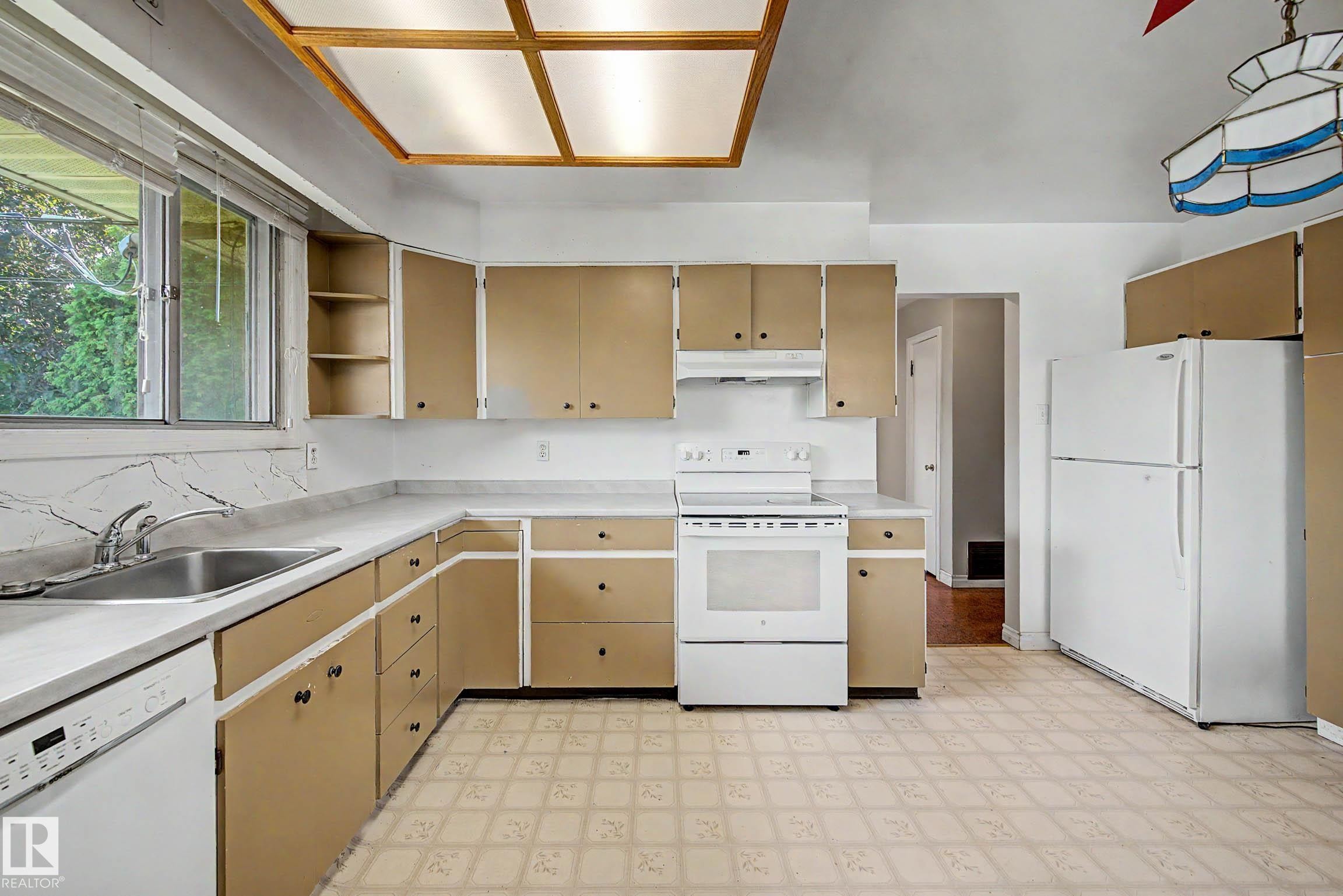 Full range of appliances, extensive cabinetry, double basin stainless steel sink, large window, and patterned flooring - 9723 76 Street Nw, Edmonton, AB - Indoor Photo Showing Kitchen