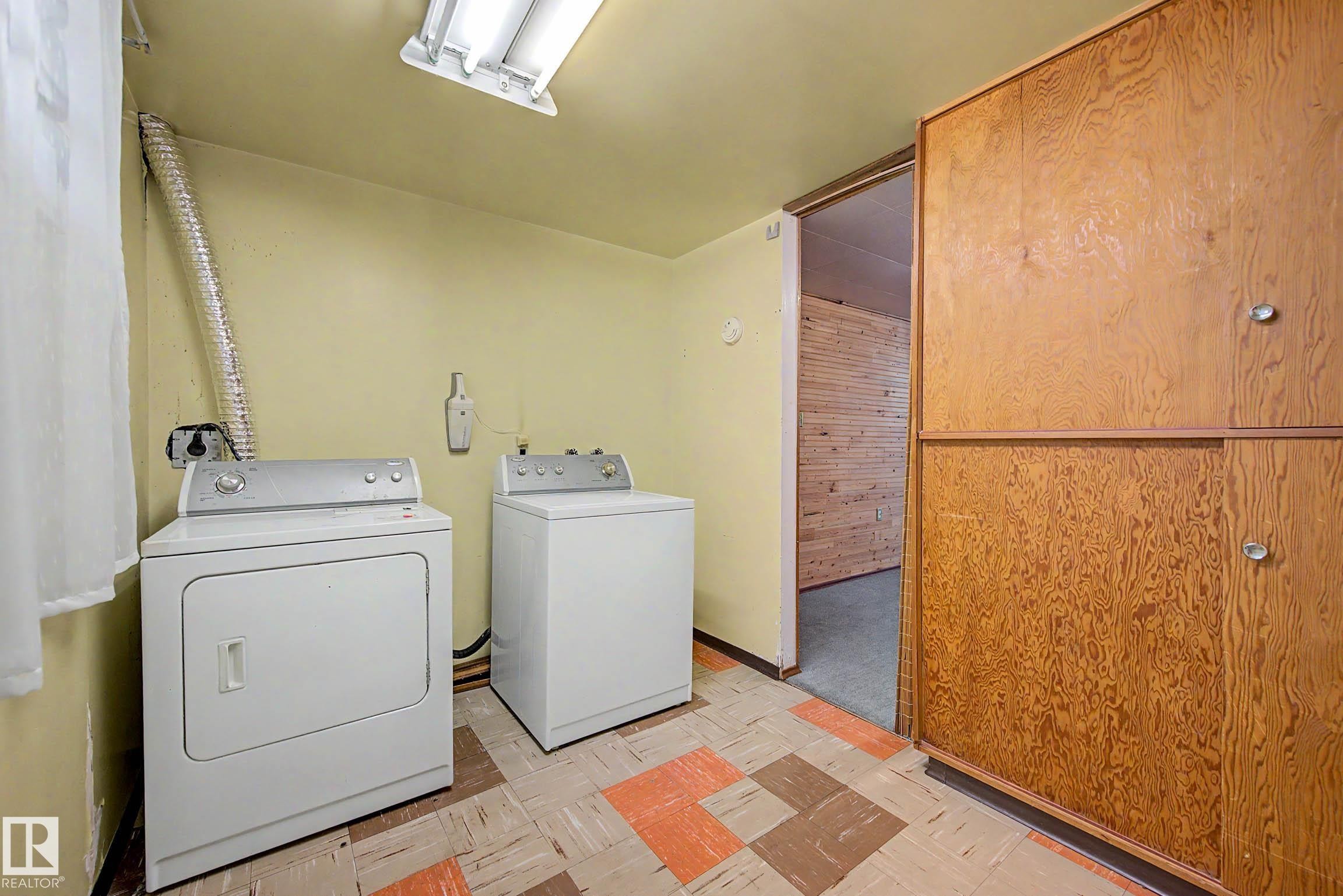 Utility area featuring a washer and dryer, built-in wood-finish cabinetry, and patterned floor tiles - 9723 76 Street Nw, Edmonton, AB - Indoor Photo Showing Laundry Room