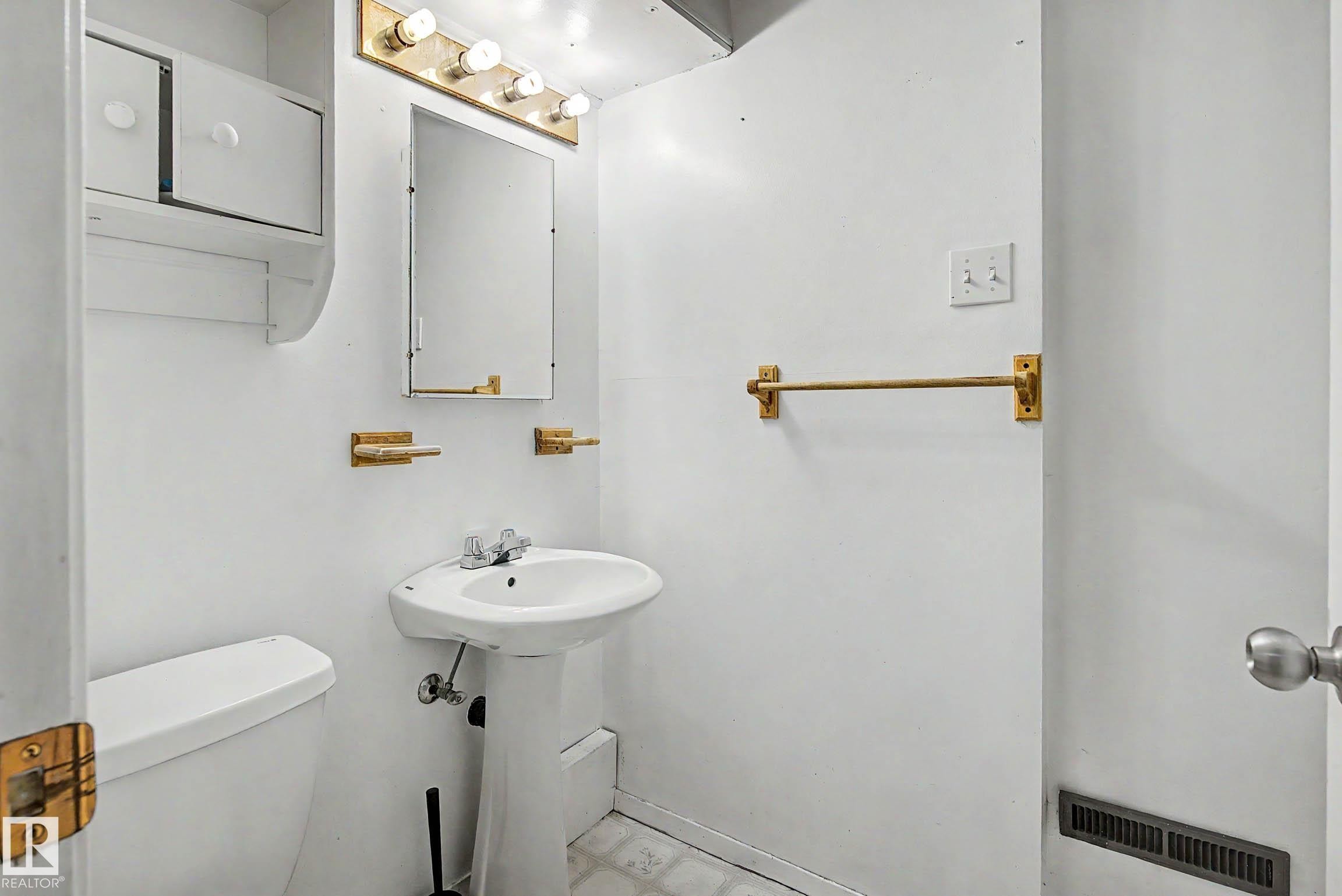 Pedestal sink with chrome-finish faucet, wall-mounted mirror, and overhead vanity lighting - 9723 76 Street Nw, Edmonton, AB - Indoor Photo Showing Bathroom