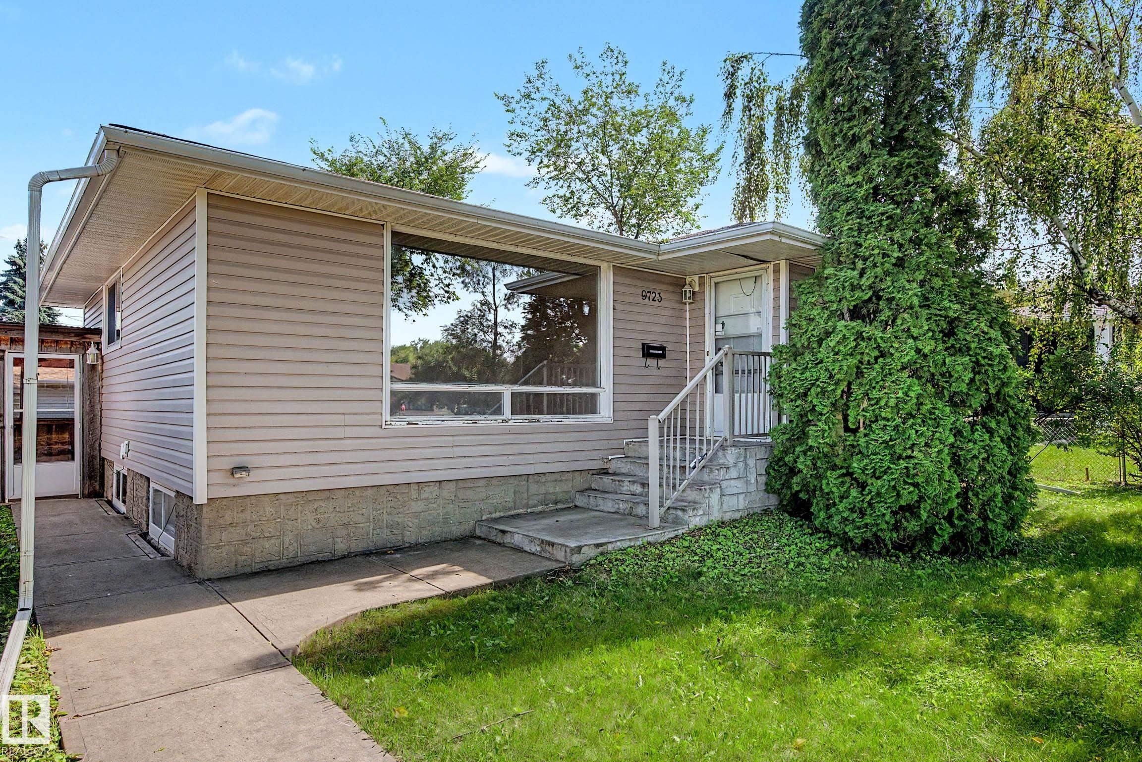 Siding exterior with a large picture window, concrete walkway, established lawn, and mature landscaping - 9723 76 Street Nw, Edmonton, AB - Outdoor