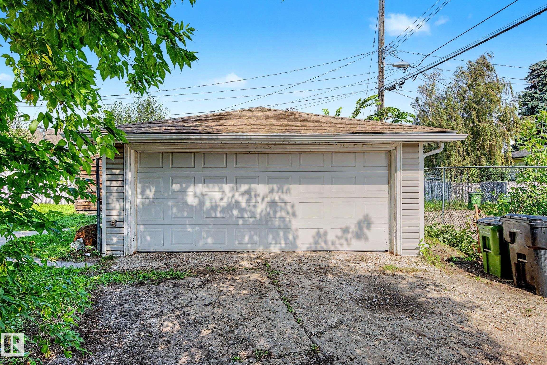 Detached garage featuring a paneled overhead door, shingle roof, and light-colored siding - 9723 76 Street Nw, Edmonton, AB - Outdoor