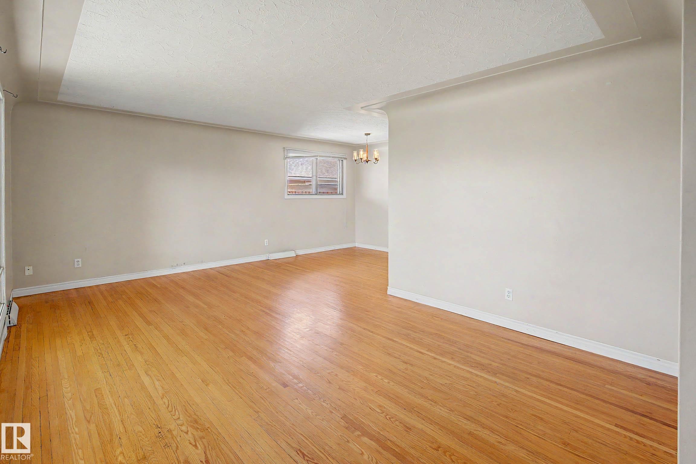 Hardwood flooring throughout, neutral wall finishes, and a chandelier lighting fixture - 9723 76 Street Nw, Edmonton, AB - Indoor Photo Showing Other Room