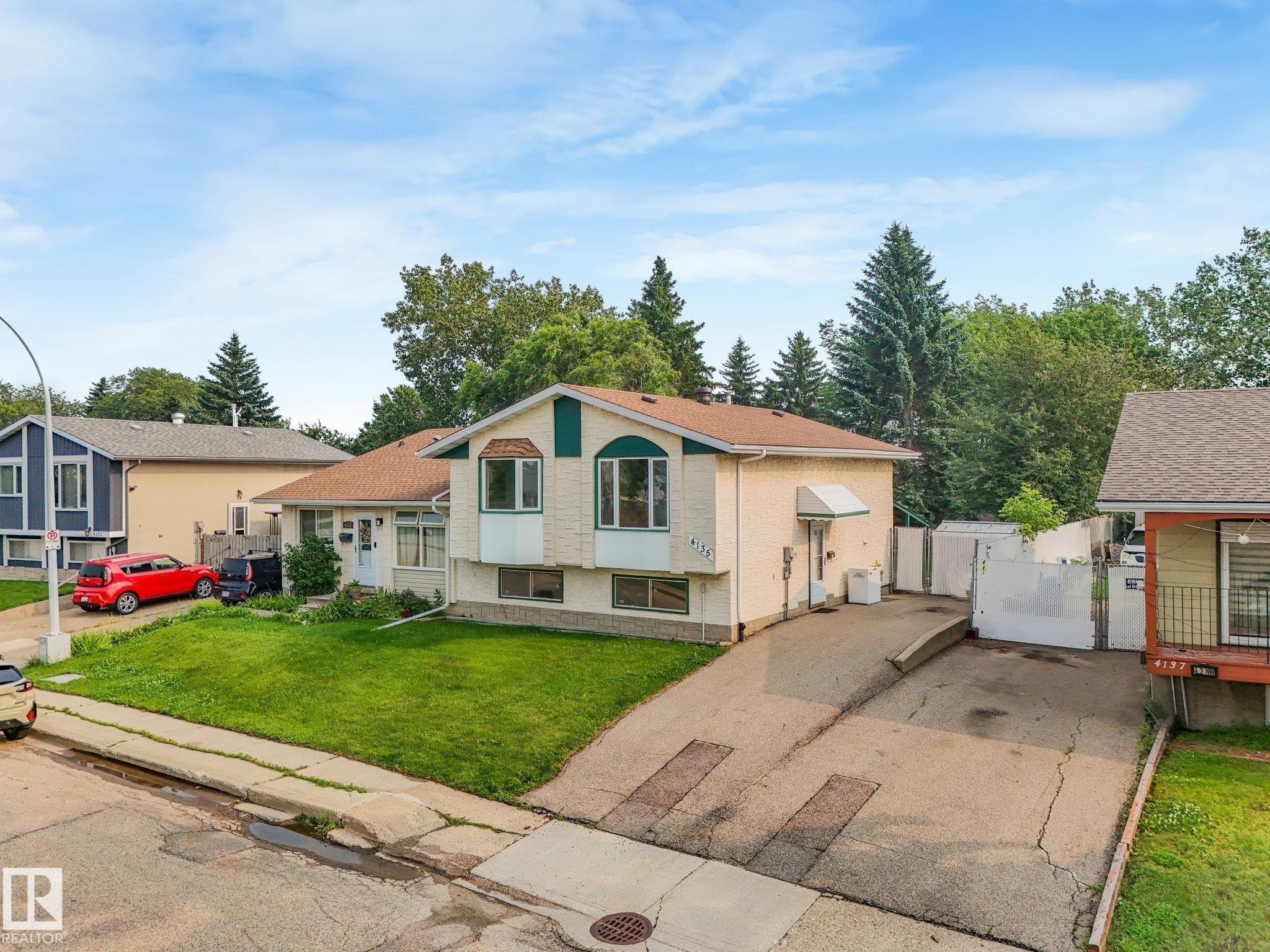 Cream-colored exterior with a green-trimmed bay window, white entry door, and a mature treeline backdrop - 4135 134 Avenue Nw, Edmonton, AB - Outdoor