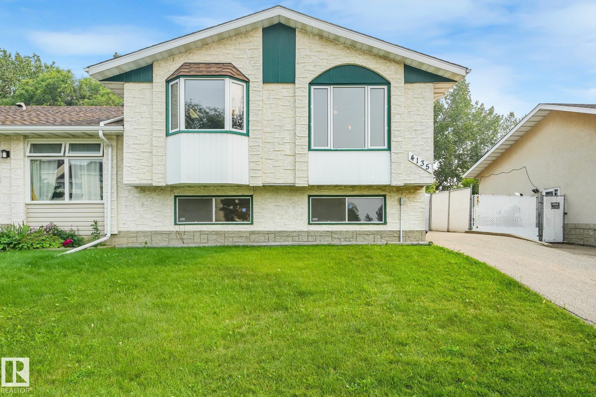 Split-level home featuring a light-colored textured exterior, a green gabled roofline, and a prominent bay window - 4135 134 Avenue Nw, Edmonton, AB - Outdoor