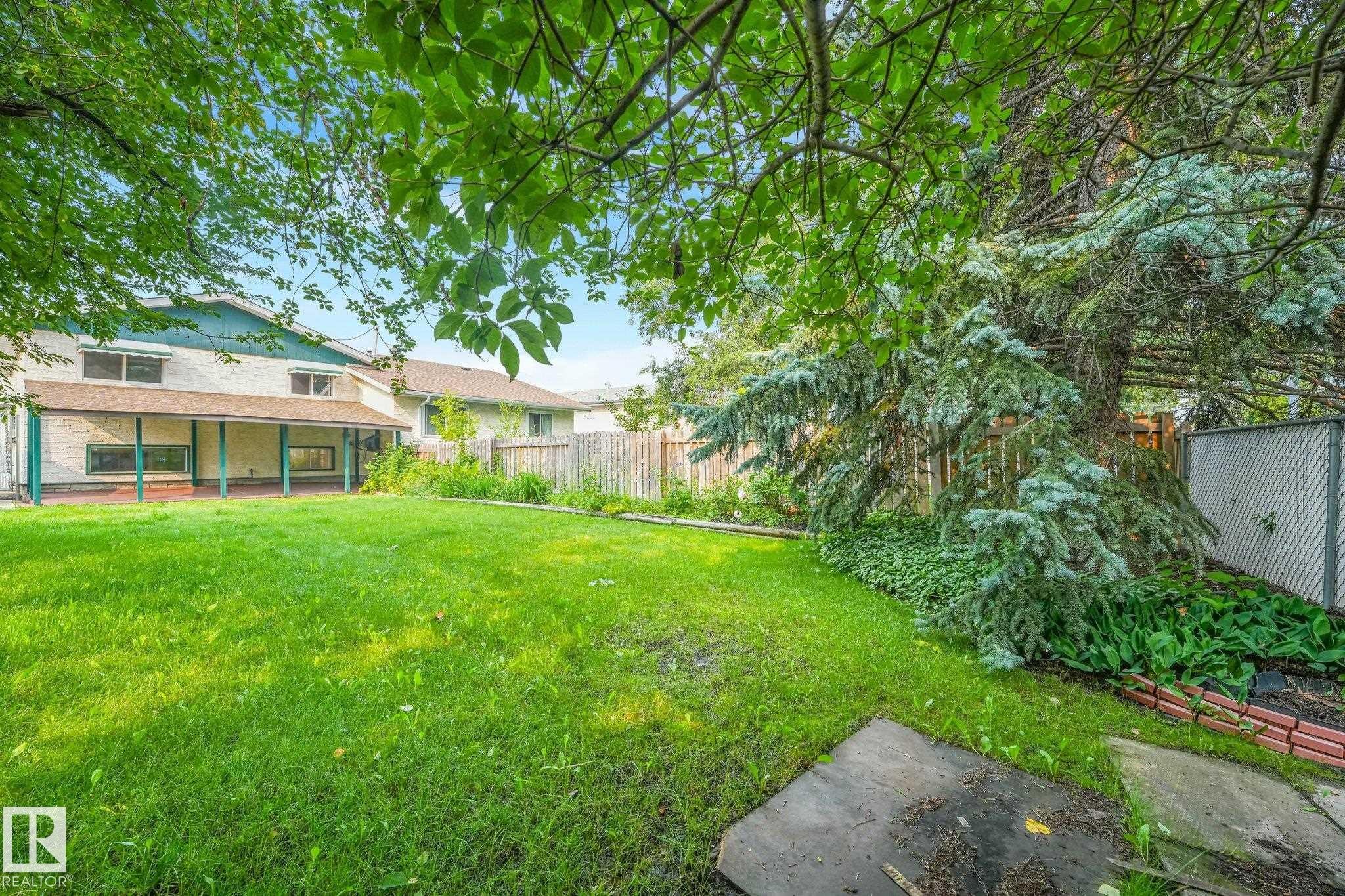 Spacious rear yard featuring an expansive lawn, mature perimeter trees, and a covered patio area with support columns - 4135 134 Avenue Nw, Edmonton, AB - Outdoor With Deck Patio Veranda