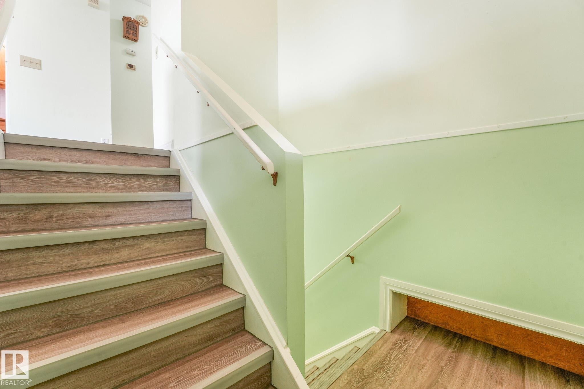 Stairwell featuring wood-finish treads with light gray risers and nosing, white handrails, and a light green lower wall panel - 4135 134 Avenue Nw, Edmonton, AB - Indoor Photo Showing Other Room