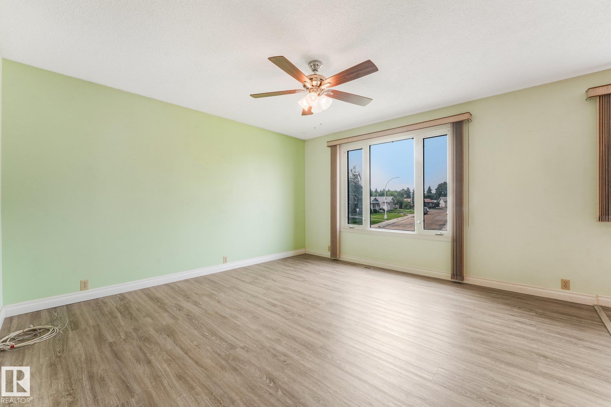 Spacious room featuring wood-finish flooring, a multi-pane window, and a ceiling fan with light fixture - 4135 134 Avenue Nw, Edmonton, AB - Indoor Photo Showing Other Room