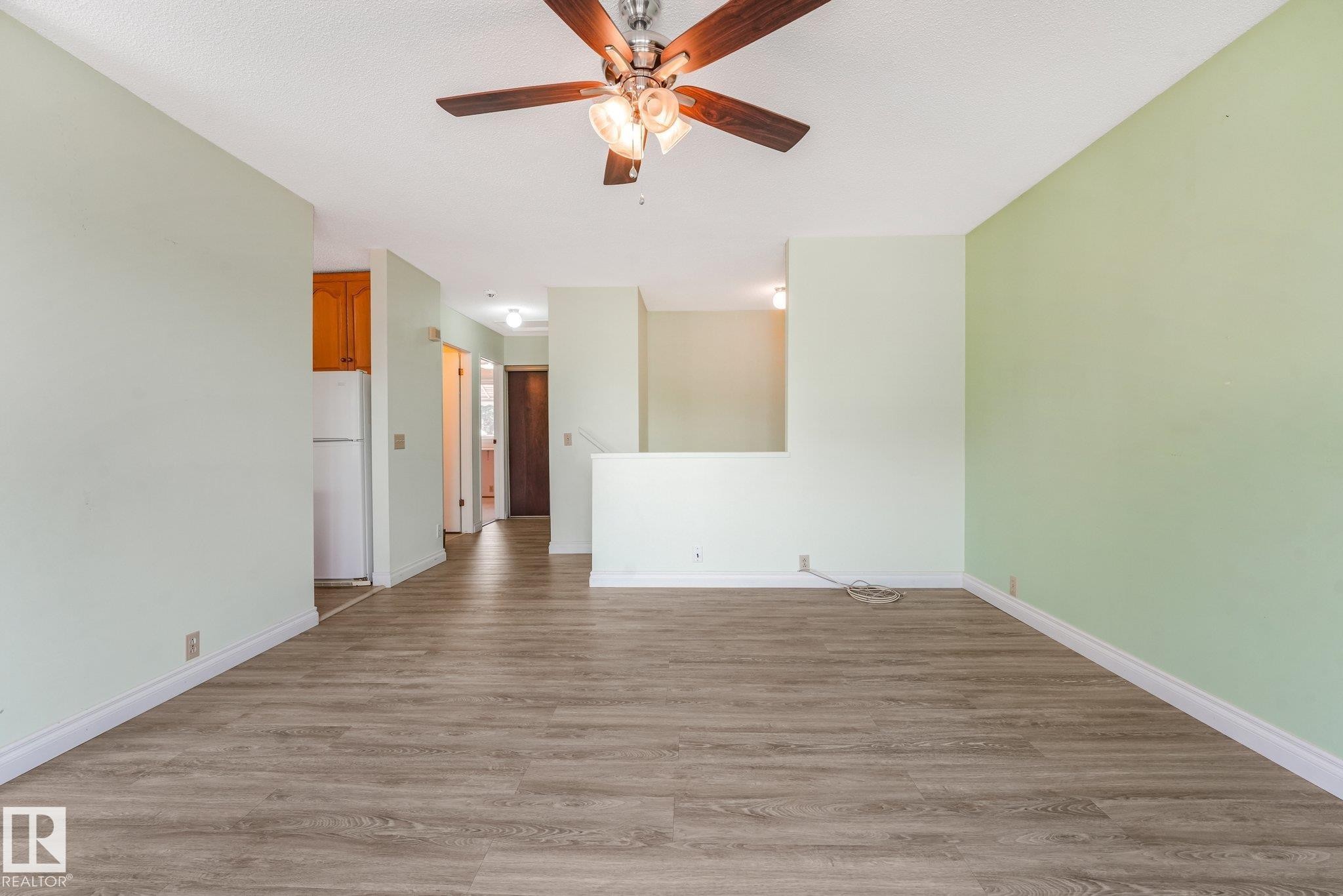 Spacious room featuring wood-finish flooring, light green walls, white baseboards, and a ceiling fan with integrated lighting - 4135 134 Avenue Nw, Edmonton, AB - Indoor Photo Showing Other Room