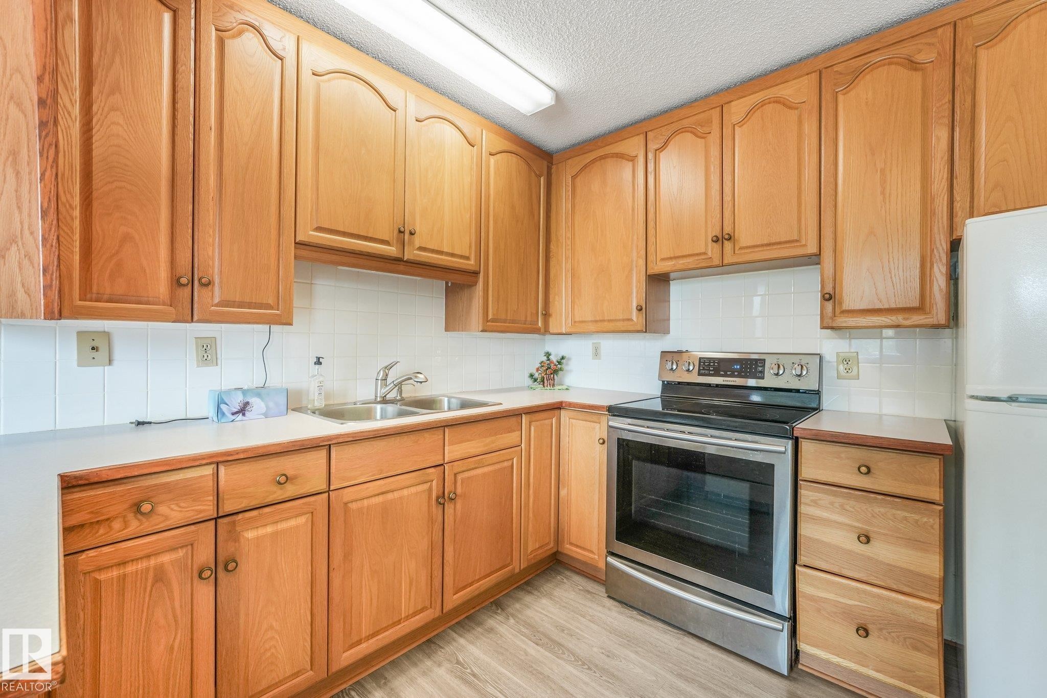 Kitchen featuring wood cabinetry, white countertops, a stainless steel range, a double basin stainless steel sink, and wood-finish flooring - 4135 134 Avenue Nw, Edmonton, AB - Indoor Photo Showing Kitchen With Double Sink