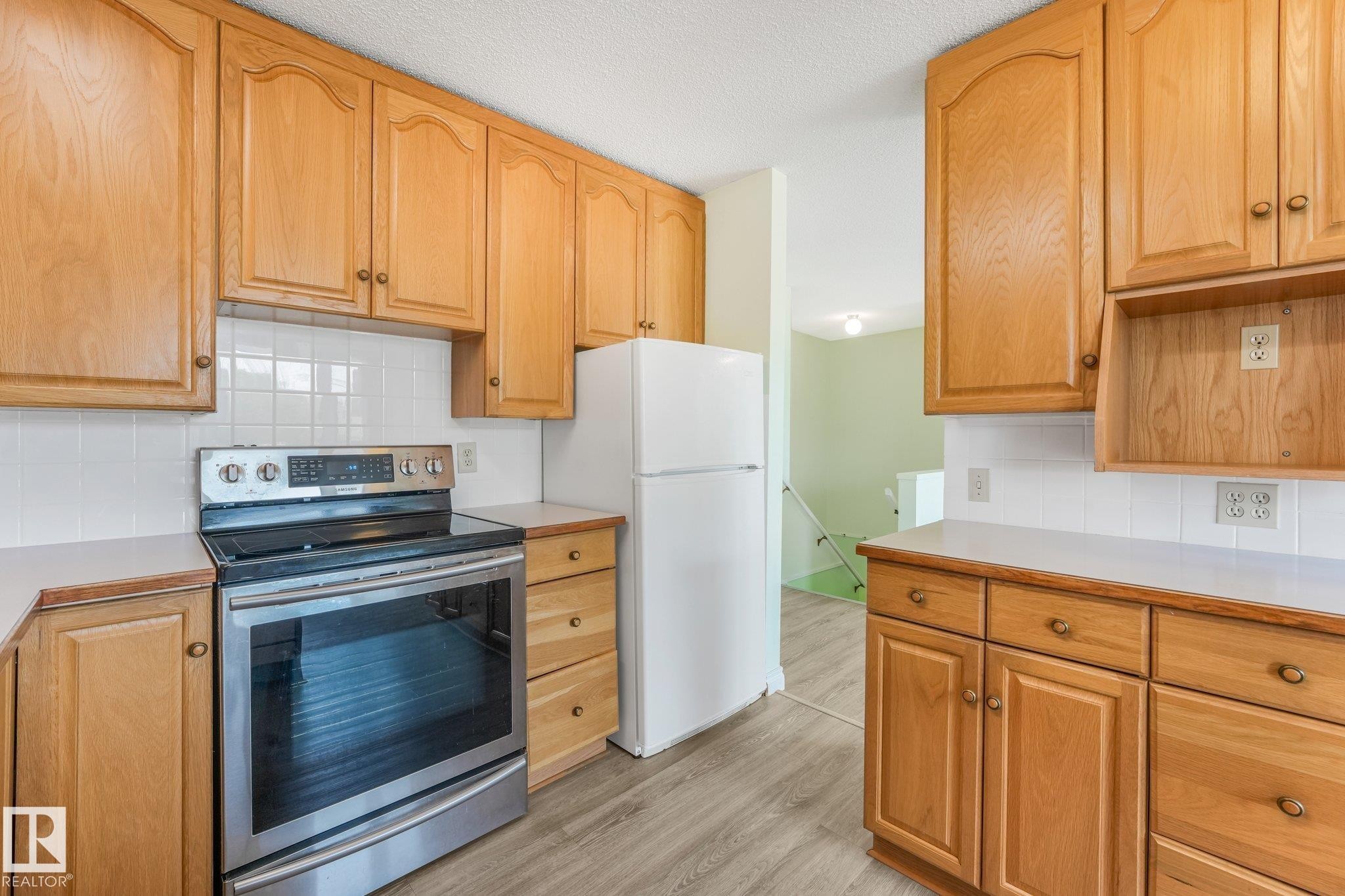 Kitchen featuring wood cabinetry, white tile backsplash, light wood-finish flooring, and white countertops - 4135 134 Avenue Nw, Edmonton, AB - Indoor Photo Showing Kitchen
