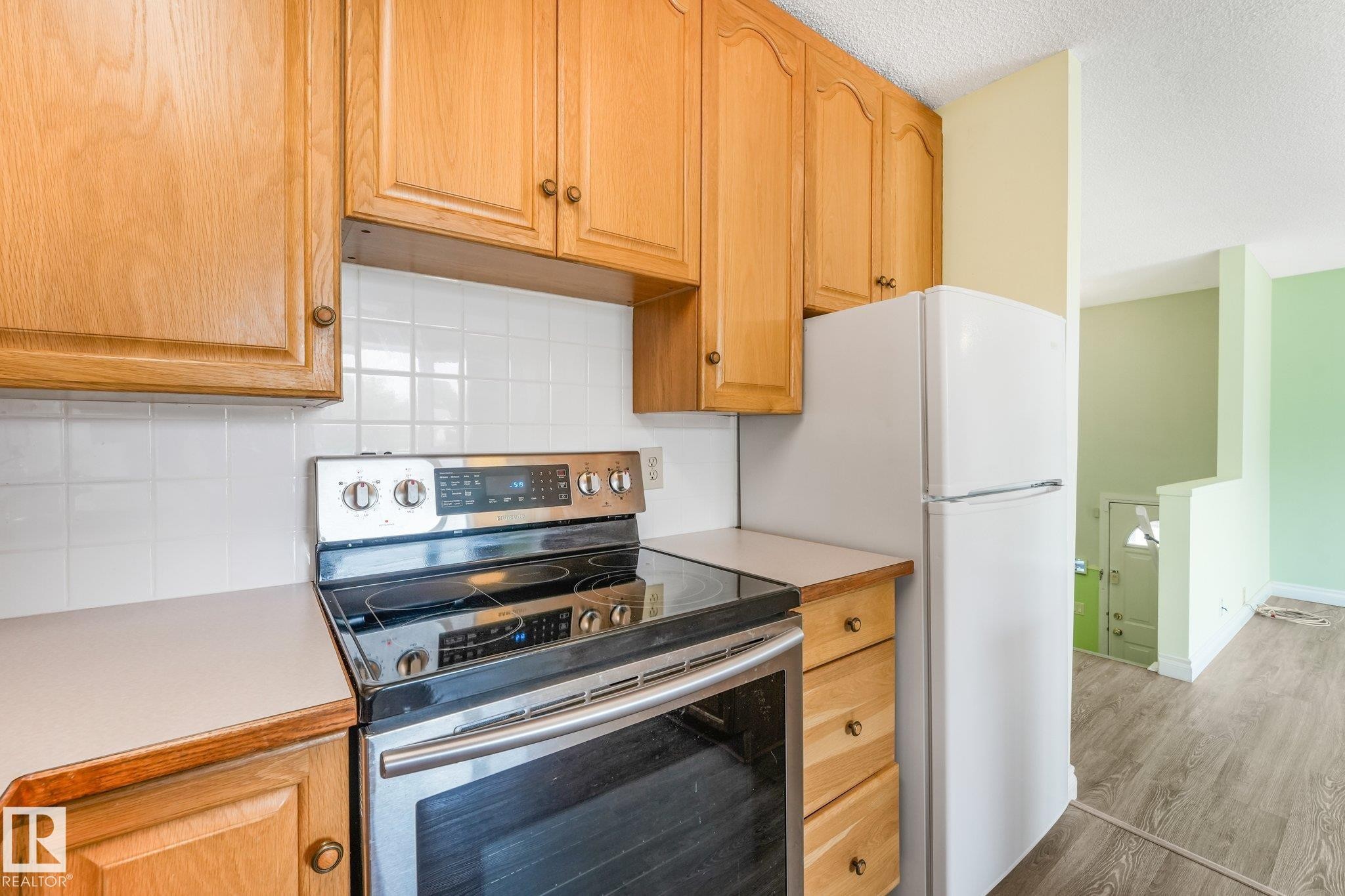 Kitchen featuring wood cabinetry, white tile backsplash, light countertops, and a stainless steel range - 4135 134 Avenue Nw, Edmonton, AB - Indoor Photo Showing Kitchen