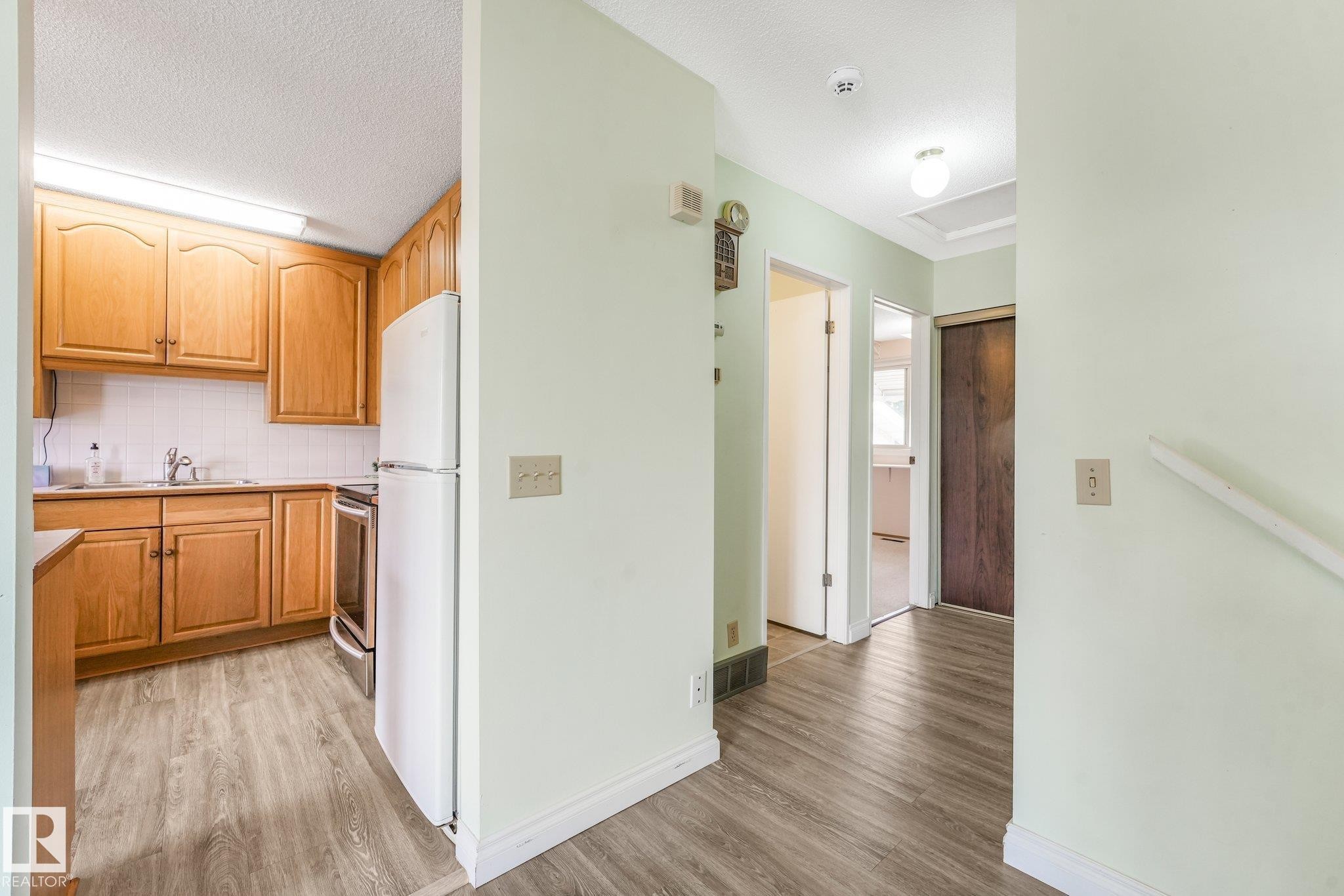 Kitchen featuring light wood cabinetry, white appliances, and wood-finish flooring - 4135 134 Avenue Nw, Edmonton, AB - Indoor