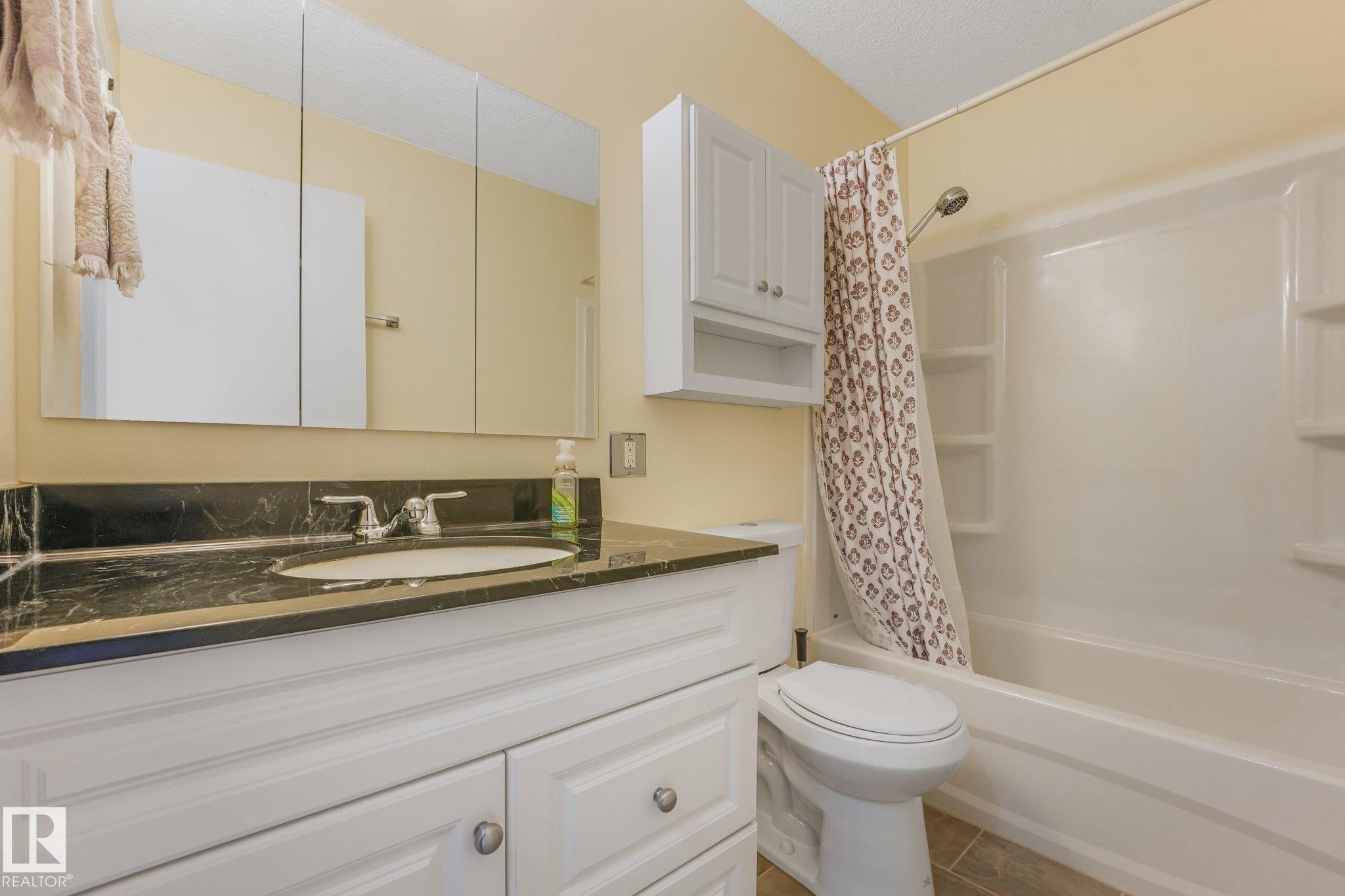 Bathroom featuring a white vanity with paneling, dark stone countertop, and an undermount sink - 4135 134 Avenue Nw, Edmonton, AB - Indoor Photo Showing Bathroom