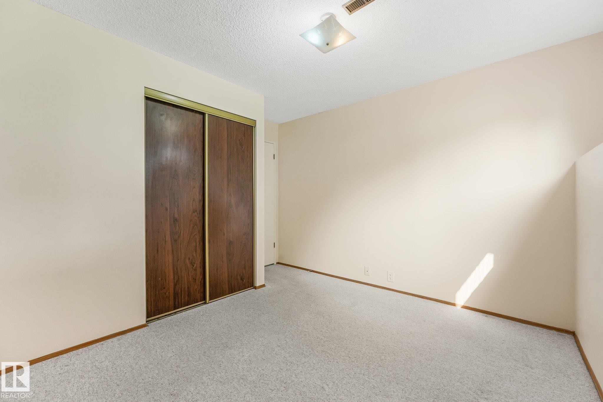 Neutral-toned room featuring a ceiling-mounted light fixture, light-colored walls, and wood-finish sliding closet doors - 4135 134 Avenue Nw, Edmonton, AB - Indoor Photo Showing Other Room