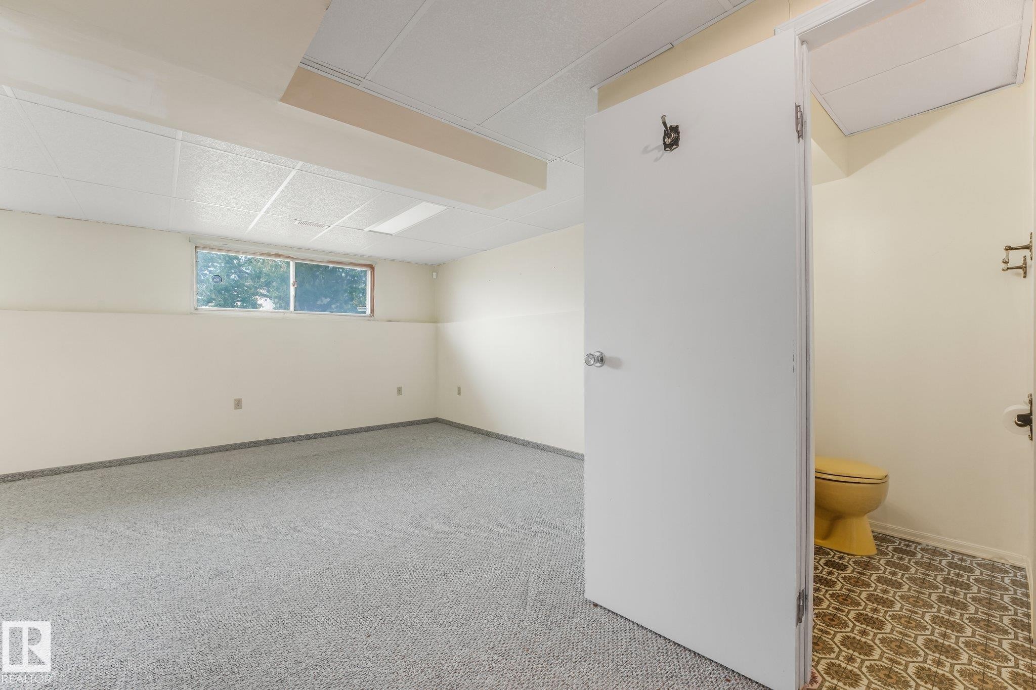 Spacious interior featuring light gray carpeting, a drop ceiling, and a single window - 4135 134 Avenue Nw, Edmonton, AB - Indoor