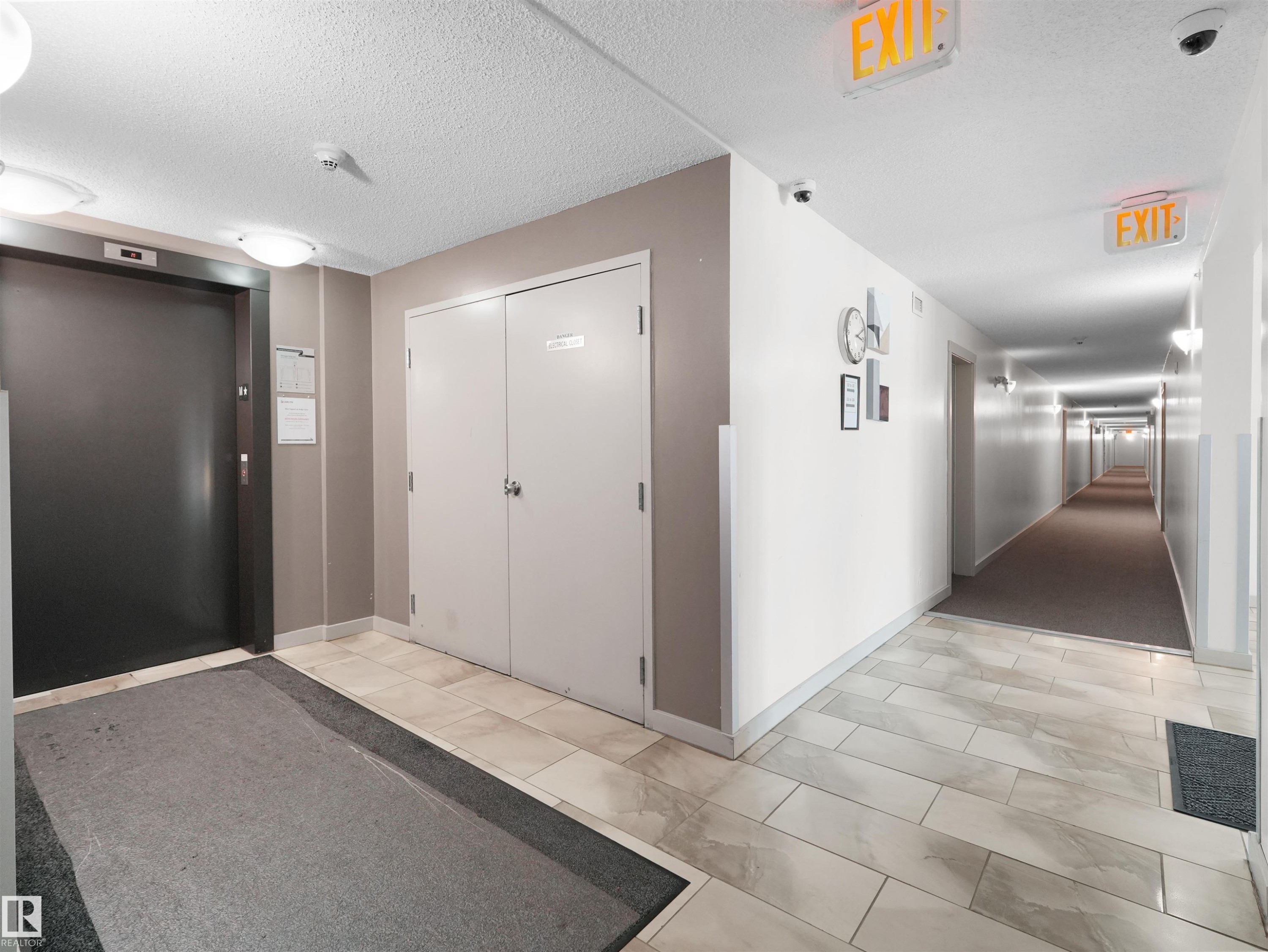 Elevator access, tile flooring, flush-mounted ceiling lights, and hallway with wall sconces - #205 5816 Mullen Pl Nw, Edmonton, AB - Indoor Photo Showing Other Room