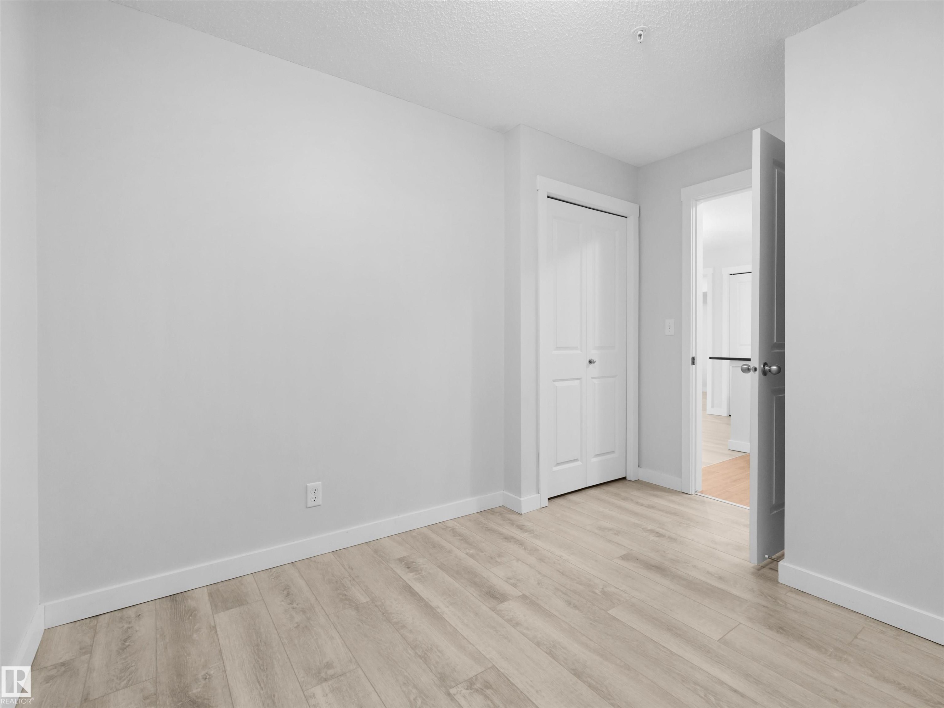 Light wood-finish flooring, white walls, and a bi-fold closet door - #205 5816 Mullen Pl Nw, Edmonton, AB - Indoor Photo Showing Other Room