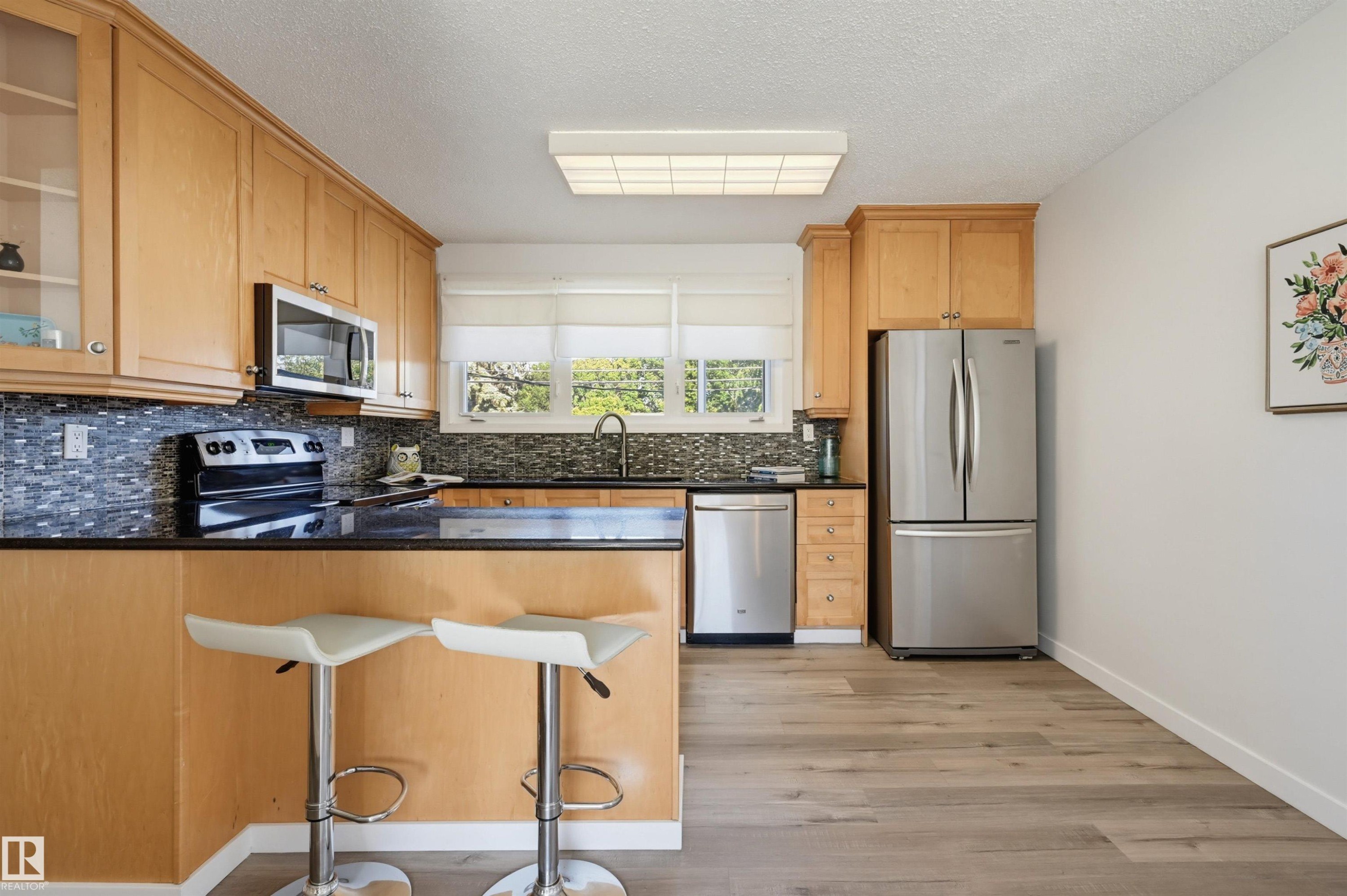 Kitchen featuring wood-finish cabinetry, stainless steel appliances, black countertops, and a tile backsplash - 9127 149 Street Nw, Edmonton, AB - Indoor Photo Showing Kitchen