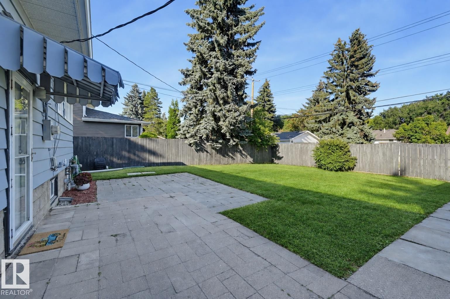 Expansive paved patio with a manicured lawn, established privacy fence, and mature trees - 9127 149 Street Nw, Edmonton, AB - Outdoor